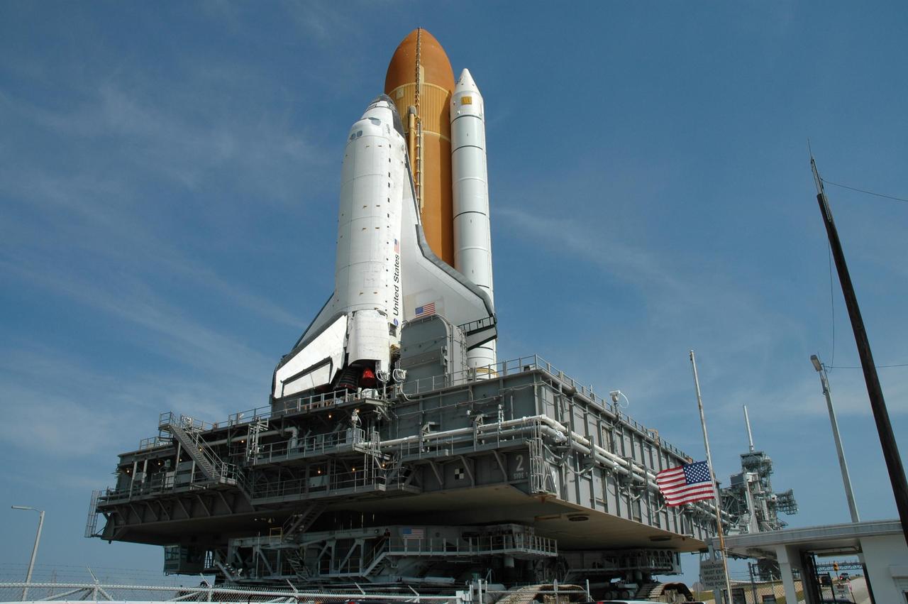 KENNEDY SPACE CENTER, FLA. --  Space Shuttle Atlantis, mounted on a mobile launch platform atop a crawler transporter, passes through the gate to Launch Pad 39A.  The flag is flying at half mast in recognition of Peace Officers Memorial Day as authorized by the President.  First motion of the shuttle out of the Vehicle Assembly Building was at 5:02 a.m. EDT. In late February, while Atlantis was on the launch pad, Atlantis' external tank received hail damage during a severe thunderstorm that passed through the Kennedy Space Center Launch Complex 39 area. The hail caused visible divots in the giant tank's foam insulation, as well as minor surface damage to about 26 heat shield tiles on the shuttle's left wing. The shuttle was returned to the VAB for repairs. The launch of Space Shuttle Atlantis on mission STS-117 is now targeted for June 8. A flight readiness review will be held on May 30 and 31.  Photo credit: NASA/Jim Grossmann