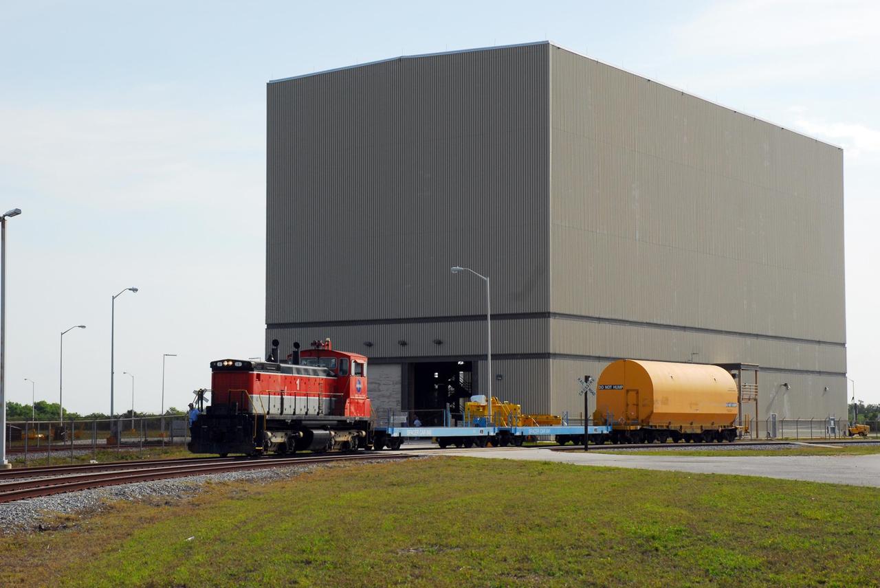 KENNEDY SPACE CENTER, FLA. --   The locomotive and rail cars carrying solid rocket booster motor segments and two aft exit cone segments deliver their cargo to the Rotation, Processing and Surge Facility (RPSF) in Kennedy Space Center's Launch Complex 39 Area.  The RPSF is used for solid rocket motor receiving, rotation and inspection, and supports aft booster buildup.  When live solid rocket motor segments arrive at the processing facility, they  are positioned under one of the cranes. Handling slings are then attached to and remove the railcar cover. The segment is inspected while it remains horizontal.  The two overhead cranes hoist the segment, rotate it to a vertical position and place it on a fixed stand. The aft handling ring is then removed. The segment is hoisted again and lowered onto a transportation and storage pallet, and the forward handling ring is removed to allow inspections. It is then transported to one of the surge buildings and temporarily stored until it is needed for booster stacking in the VAB.  While enroute, solid rocket motor segments were involved in a derailment in Alabama.  The rail cars carrying these segments remained upright and were undamaged.  An inspection determined these segment cars could continue on to Florida.  The segments themselves will undergo further evaluation at Kennedy before they are cleared for flight.  Other segments involved in the derailment will be returned to a plant in Utah for further evaluation.  Photo credit: NASA/George Shelton