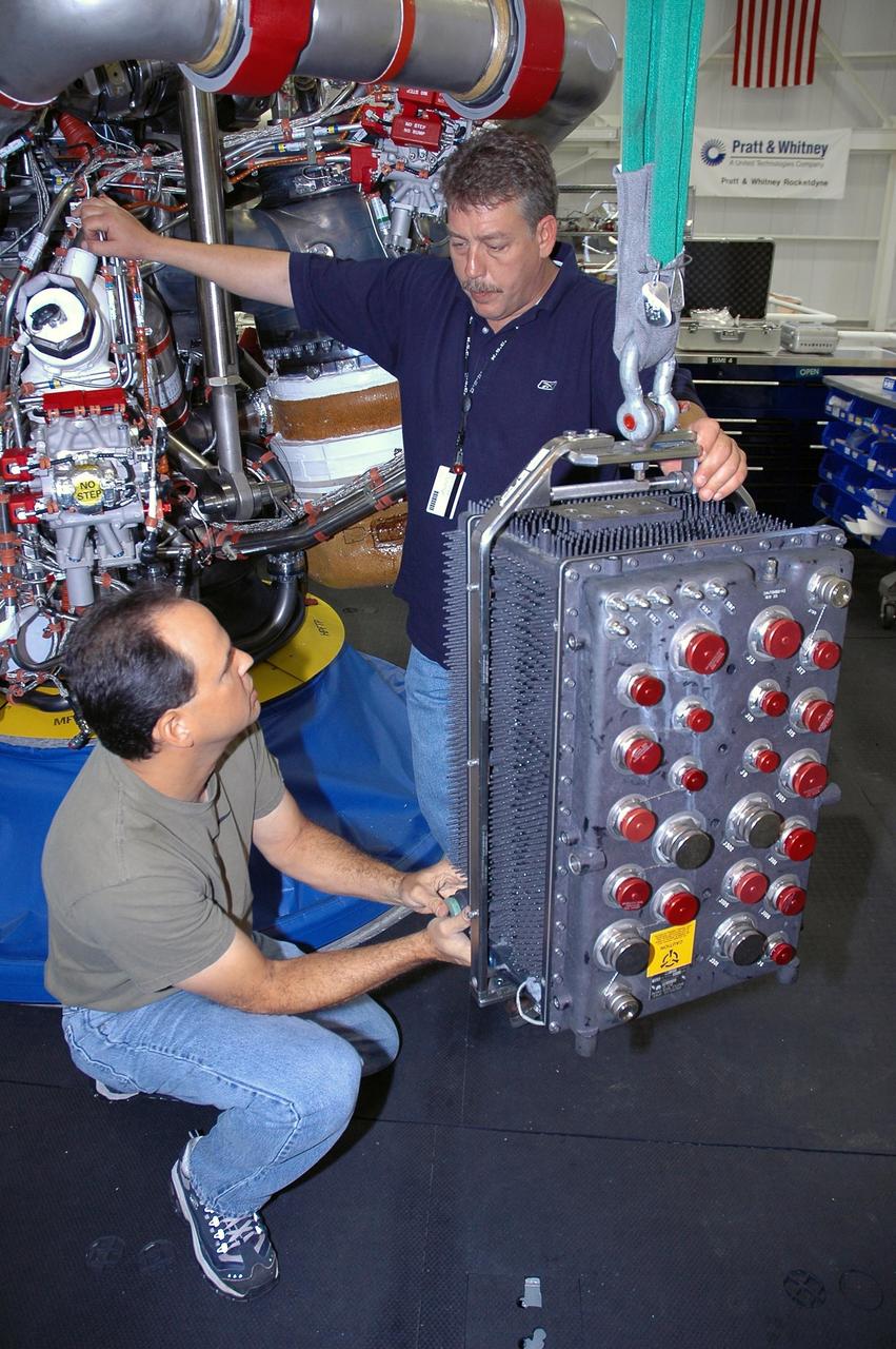 KENNEDY SPACE CENTER, FLA. --   In Space Shuttle Maine Engine Shop, workers get ready to install an engine controller in one of the three main engines (behind them) of the orbiter Discovery.  The controller is an electronics package mounted on each space shuttle main engine. It contains two digital computers and the associated electronics to control all main engine components and operations. The controller is attached to the main combustion chamber by shock-mounted fittings.  Discovery is the designated orbiter for mission STS-120 to the International Space Station.  It will carry a payload that includes the Node 2 module, named Harmony. Launch is targeted for no earlier than Oct. 20.   Photo credit: NASA/Cory Huston