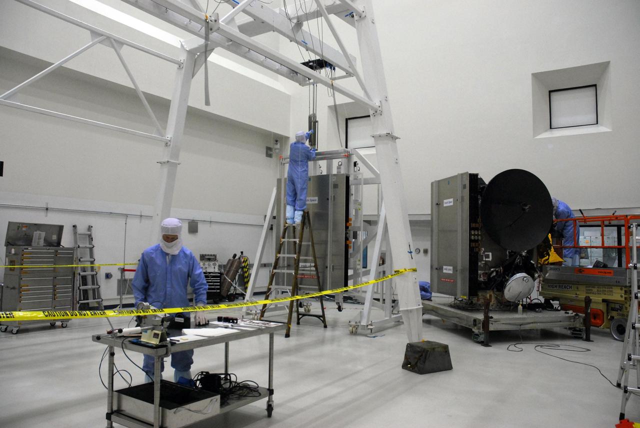 KENNEDY SPACE CENTER, FLA. --    At Astrotech, workers (in the background) secure a crane onto a set of solar array panels that will be installed on the Dawn spacecraft, at right.  Another set was installed previously. Together, the panels extend 64.6 feet when fully open.Dawn is scheduled to launch June 30 aboard a Delta II rocket from Launch Complex 17-B at Cape Canaveral Air Force Station.   Dawn's mission is to explore two of the asteroid belt's most intriguing and dissimilar occupants: asteroid Vesta and the dwarf planet Ceres.  Photo credit: NASA/George Shelton