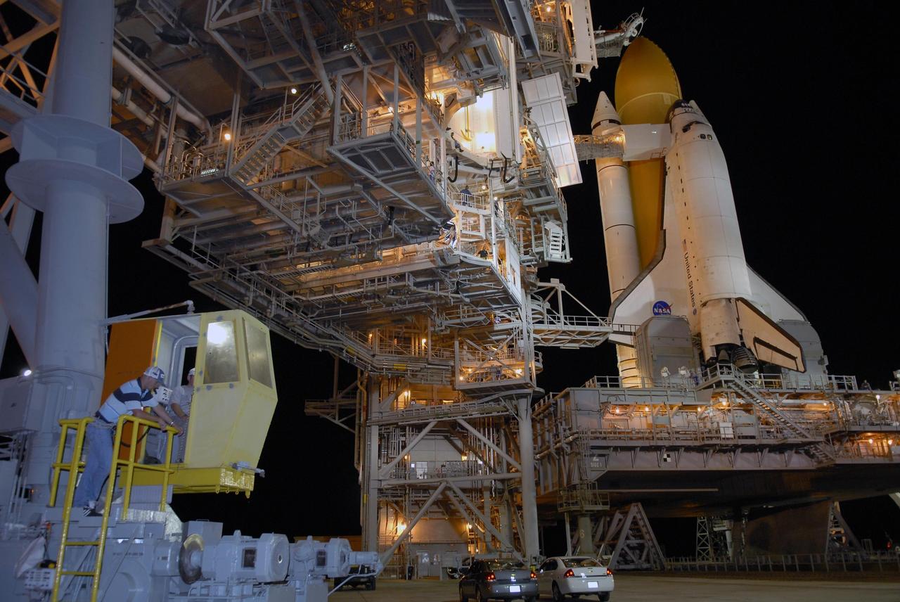 KENNEDY SPACE CENTER, FLA. --  At Launch Pad 39A, Space Shuttle Atlantis stands bathed in lights atop a mobile launch platform as technicians in the control booth roll the rotating service structure, or RSS, away from the orbiter. Rollback is one of the milestones in preparation for the launch of mission STS-117 on June 8. Rollback started at 10:56 p.m. and was complete at 11:34 p.m EDT. The RSS provides protected access to the orbiter for changeout and servicing of payloads at the pad. The structure is supported by a rotating bridge that pivots about a vertical axis on the side of the pad's flame trench. The hinge column rests on the pad surface and is braced to the fixed service structure.  Support for the outer end of the bridge is provided by two eight-wheel, motor-driven trucks that move along circular twin rails installed flush with the pad surface. The track crosses the flame trench on a permanent bridge. The RSS is 102 feet long, 50 feet wide and 130 feet high. The structure has orbiter access platforms at five levels to provide access to the payload bay while the orbiter is being serviced in the RSS. Each platform has independent extendable planks that can be arranged to conform to a payload's configuration. This mission is the 118th shuttle flight and the 21st U.S. flight to the International Space Station and will deliver and install the S3/S4 truss segment, deploy a set of solar arrays and prepare them for operation.  Photo credit: NASA/Kim Shiflett