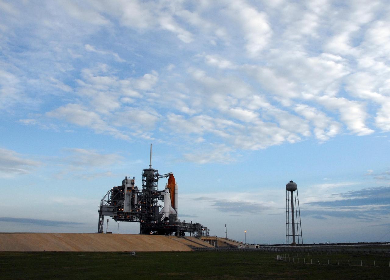 KENNEDY SPACE CENTER, FLA. -- The sun rises on a cloudy Florida day to reveal Space Shuttle Atlantis awaiting launch atop a mobile launch platform at Launch Pad 39A. Rollback of the pad's rotating service structure, or RSS, is one of the milestones in preparation for the launch of mission STS-117 on June 8. Rollback started at 10:56 p.m. EDT June 7 and was complete at 11:34 p.m. The RSS, the massive structure to the left of the shuttle, provides protected access to the orbiter for changeout and servicing of payloads at the pad. The structure is supported by a rotating bridge that pivots about a vertical axis on the side of the pad's flame trench. The hinge column rests on the pad surface and is braced to the fixed service structure. Support for the outer end of the bridge is provided by two eight-wheel, motor-driven trucks that move along circular twin rails installed flush with the pad surface. The track crosses the flame trench on a permanent bridge. The RSS is 102 feet long, 50 feet wide and 130 feet high. The structure has orbiter access platforms at five levels to provide access to the payload bay while the orbiter is being serviced in the RSS. Each platform has independent extendable planks that can be arranged to conform to a payload's configuration. This mission is the 118th shuttle flight and the 21st U.S. flight to the International Space Station and will deliver and install the S3/S4 truss segment, deploy a set of solar arrays and prepare them for operation. Photo credit: NASA/Ken Thornsley