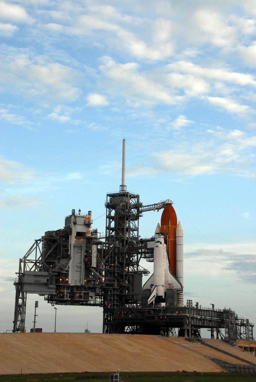 KENNEDY SPACE CENTER, FLA. -- Following sunrise on a cloudy Florida day, Space Shuttle Atlantis awaits launch atop a mobile launch platform at Launch Pad 39A. Rollback of the pad's rotating service structure, or RSS, is one of the milestones in preparation for the launch of mission STS-117 on June 8. Rollback started at 10:56 p.m. EDT June 7 and was complete at 11:34 p.m. The RSS, the massive structure to the left of the shuttle, provides protected access to the orbiter for changeout and servicing of payloads at the pad. The structure is supported by a rotating bridge that pivots about a vertical axis on the side of the pad's flame trench. The hinge column rests on the pad surface and is braced to the fixed service structure. Support for the outer end of the bridge is provided by two eight-wheel, motor-driven trucks that move along circular twin rails installed flush with the pad surface. The track crosses the flame trench on a permanent bridge. The RSS is 102 feet long, 50 feet wide and 130 feet high. The structure has orbiter access platforms at five levels to provide access to the payload bay while the orbiter is being serviced in the RSS. Each platform has independent extendable planks that can be arranged to conform to a payload's configuration. This mission is the 118th shuttle flight and the 21st U.S. flight to the International Space Station and will deliver and install the S3/S4 truss segment, deploy a set of solar arrays and prepare them for operation. Photo credit: NASA/Ken Thornsley
