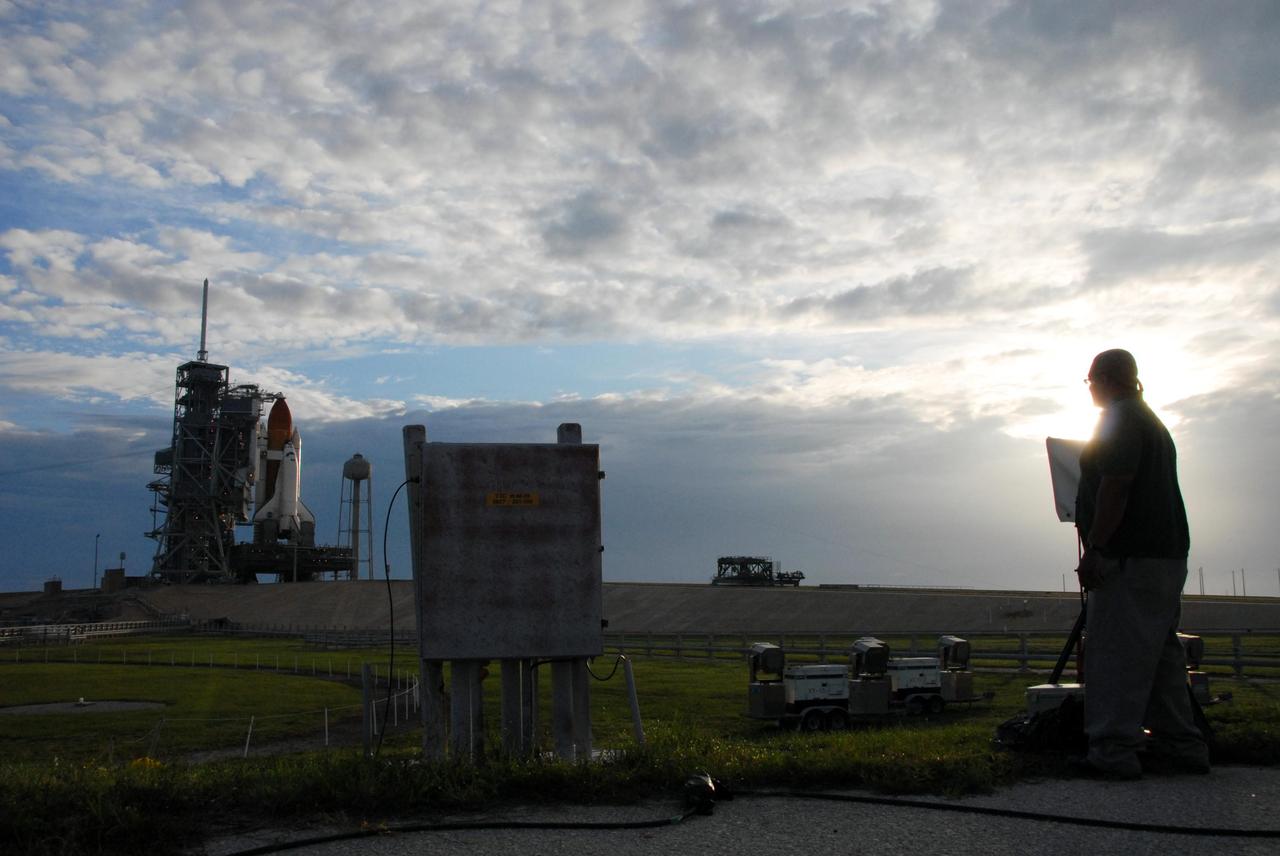 KENNEDY SPACE CENTER, FLA. -- Cameras are prepared to record the launch of Space Shuttle Atlantis from Launch Pad 39A by Theaphlias B. Terrell, operations manager of Bionetics Photoservice, following sunrise on a cloudy Florida day. Rollback of the pad's rotating service structure, or RSS, is one of the milestones in preparation for the launch of mission STS-117 on June 8. Rollback started at 10:56 p.m. EDT June 7 and was complete at 11:34 p.m. The RSS, the massive structure to the left of the shuttle, provides protected access to the orbiter for changeout and servicing of payloads at the pad. The structure is supported by a rotating bridge that pivots about a vertical axis on the side of the pad's flame trench. The hinge column rests on the pad surface and is braced to the fixed service structure. Support for the outer end of the bridge is provided by two eight-wheel, motor-driven trucks that move along circular twin rails installed flush with the pad surface. The track crosses the flame trench on a permanent bridge. The RSS is 102 feet long, 50 feet wide and 130 feet high. The structure has orbiter access platforms at five levels to provide access to the payload bay while the orbiter is being serviced in the RSS. Each platform has independent extendable planks that can be arranged to conform to a payload's configuration. This mission is the 118th shuttle flight and the 21st U.S. flight to the International Space Station and will deliver and install the S3/S4 truss segment, deploy a set of solar arrays and prepare them for operation. Photo credit: NASA/Ken Thornsley