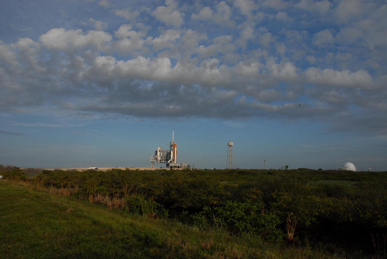 KENNEDY SPACE CENTER, FLA. -- The sun rises on a cloudy Florida day to reveal Space Shuttle Atlantis awaiting launch atop a mobile launch platform at Launch Pad 39A. At the right of the pad is the 300,000-gallon water tank that is part of the sound suppression system during launches. Rollback of the pad's rotating service structure, or RSS, is one of the milestones in preparation for the launch of mission STS-117 on June 8. Rollback started at 10:56 p.m. EDT June 7 and was complete at 11:34 p.m. The RSS, the massive structure to the left of the shuttle, provides protected access to the orbiter for changeout and servicing of payloads at the pad. The structure is supported by a rotating bridge that pivots about a vertical axis on the side of the pad's flame trench. The hinge column rests on the pad surface and is braced to the fixed service structure. Support for the outer end of the bridge is provided by two eight-wheel, motor-driven trucks that move along circular twin rails installed flush with the pad surface. The track crosses the flame trench on a permanent bridge. The RSS is 102 feet long, 50 feet wide and 130 feet high. The structure has orbiter access platforms at five levels to provide access to the payload bay while the orbiter is being serviced in the RSS. Each platform has independent extendable planks that can be arranged to conform to a payload's configuration. This mission is the 118th shuttle flight and the 21st U.S. flight to the International Space Station and will deliver and install the S3/S4 truss segment, deploy a set of solar arrays and prepare them for operation. Photo credit: NASA/Ken Thornsley