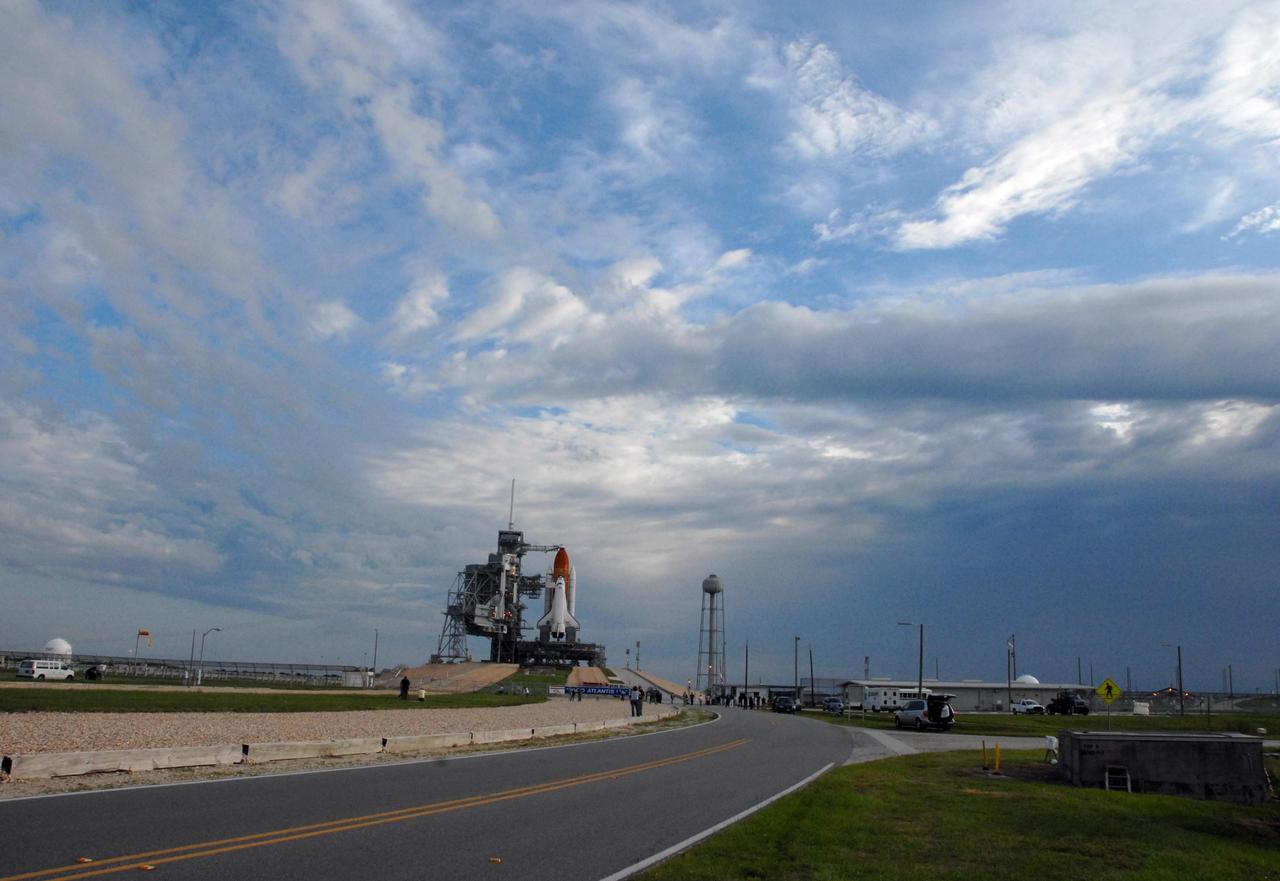KENNEDY SPACE CENTER, FLA. -- On a cloudy Florida day, Space Shuttle Atlantis awaits launch atop a mobile launch platform at Launch Pad 39A. At the right of the pad is the 290-foot tall, 300,000-gallon water tank that is part of the sound suppression system during launches. In the foreground is the crawlerway. a 130-foot-wide roadway with a 5-percent grade leading to the top of the launch pad. Rollback of the pad's rotating service structure, or RSS, is one of the milestones in preparation for the launch of mission STS-117 on June 8. Rollback started at 10:56 p.m. EDT June 7 and was complete at 11:34 p.m. The RSS, the massive structure to the left of the shuttle, provides protected access to the orbiter for changeout and servicing of payloads at the pad. The structure is supported by a rotating bridge that pivots about a vertical axis on the side of the pad's flame trench. The hinge column rests on the pad surface and is braced to the fixed service structure. Support for the outer end of the bridge is provided by two eight-wheel, motor-driven trucks that move along circular twin rails installed flush with the pad surface. The track crosses the flame trench on a permanent bridge. The RSS is 102 feet long, 50 feet wide and 130 feet high. The structure has orbiter access platforms at five levels to provide access to the payload bay while the orbiter is being serviced in the RSS. Each platform has independent extendable planks that can be arranged to conform to a payload's configuration. This mission is the 118th shuttle flight and the 21st U.S. flight to the International Space Station and will deliver and install the S3/S4 truss segment, deploy a set of solar arrays and prepare them for operation. Photo credit: NASA/Ken Thornsley