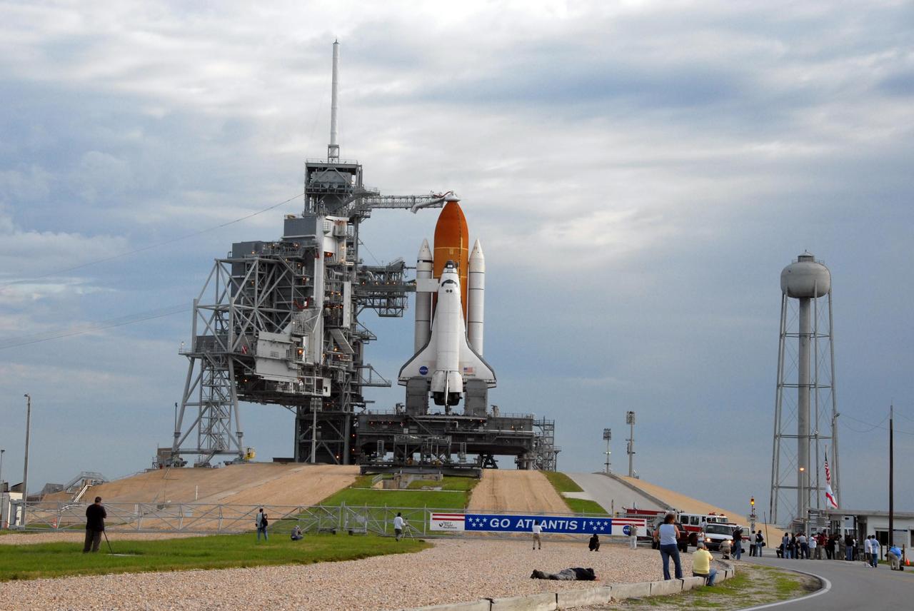 KENNEDY SPACE CENTER, FLA. -- On a cloudy Florida day, Space Shuttle Atlantis awaits launch atop a mobile launch platform at Launch Pad 39A. At the right of the pad is the 290-foot tall, 300,000-gallon water tank that is part of the sound suppression system during launches. In the foreground, photographers position themselves on the crawlerway, in hopes of capturing a unique prelaunch image. Rollback of the pad's rotating service structure, or RSS, is one of the milestones in preparation for the launch of mission STS-117 on June 8. Rollback started at 10:56 p.m. EDT June 7 and was complete at 11:34 p.m. The RSS, the massive structure to the left of the shuttle, provides protected access to the orbiter for changeout and servicing of payloads at the pad. The structure is supported by a rotating bridge that pivots about a vertical axis on the side of the pad's flame trench. The hinge column rests on the pad surface and is braced to the fixed service structure. Support for the outer end of the bridge is provided by two eight-wheel, motor-driven trucks that move along circular twin rails installed flush with the pad surface. The track crosses the flame trench on a permanent bridge. The RSS is 102 feet long, 50 feet wide and 130 feet high. The structure has orbiter access platforms at five levels to provide access to the payload bay while the orbiter is being serviced in the RSS. Each platform has independent extendable planks that can be arranged to conform to a payload's configuration. This mission is the 118th shuttle flight and the 21st U.S. flight to the International Space Station and will deliver and install the S3/S4 truss segment, deploy a set of solar arrays and prepare them for operation. Photo credit: NASA/Ken Thornsley