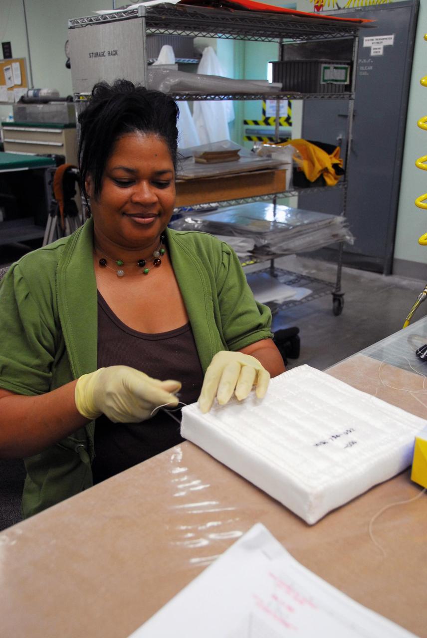 KENNEDY SPACE CENTER, FLA. --  A United Space Alliance employee prepares a test article that will be used in wind tunnel testing by NASA to collect data for analysis of the detached Flexible Insulation Blanket, or FIB, on Atlantis.  A tear occurred in an area of the OMS pod on Atlantis during launch of mission STS-117 on June 8, 2007.  The test articles each feature three tiles (Low Temperature Reusable Surface Insulation, or LRSI) affixed next to two FIB blankets, simulating the thermal protection system set-up on Atlantis' OMS pod in the vicinity of the in-flight anomaly.  These test articles will be flown to Texas the morning of June 14.  The TPS team at KSC has also provided a total of 22 FIB samples for other testing and analysis. Repair is under consideration following testing at KSC and Houston.  Photo credit: NASA/Amanda Diller