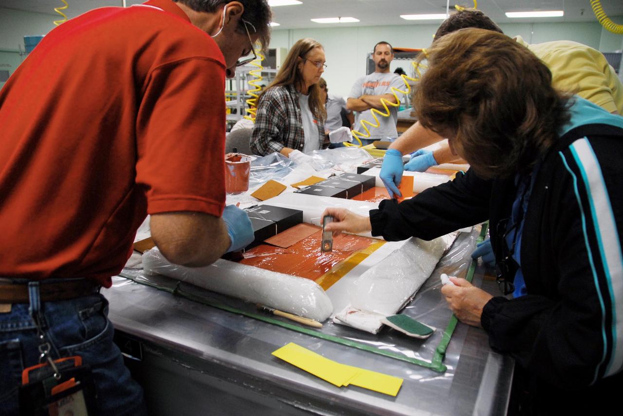 KENNEDY SPACE CENTER, FLA. --   United Space Alliance employees prepare test articles to be used in wind tunnel testing by NASA to collect data for analysis of the detached Flexible Insulation Blanket, or FIB, on Atlantis.   A tear occurred in an area of the OMS pod on Atlantis during launch of mission STS-117 on June 8, 2007.  The test articles each feature three tiles (Low Temperature Reusable Surface Insulation, or LRSI) affixed next to two FIB blankets, simulating the thermal protection system set-up on Atlantis' OMS pod in the vicinity of the in-flight anomaly.  These test articles will be flown to Texas the morning of June 14.  The TPS team at KSC has also provided a total of 22 FIB samples for other testing and analysis. Repair is under consideration following testing at KSC and Houston.  Photo credit: NASA/Amanda Diller