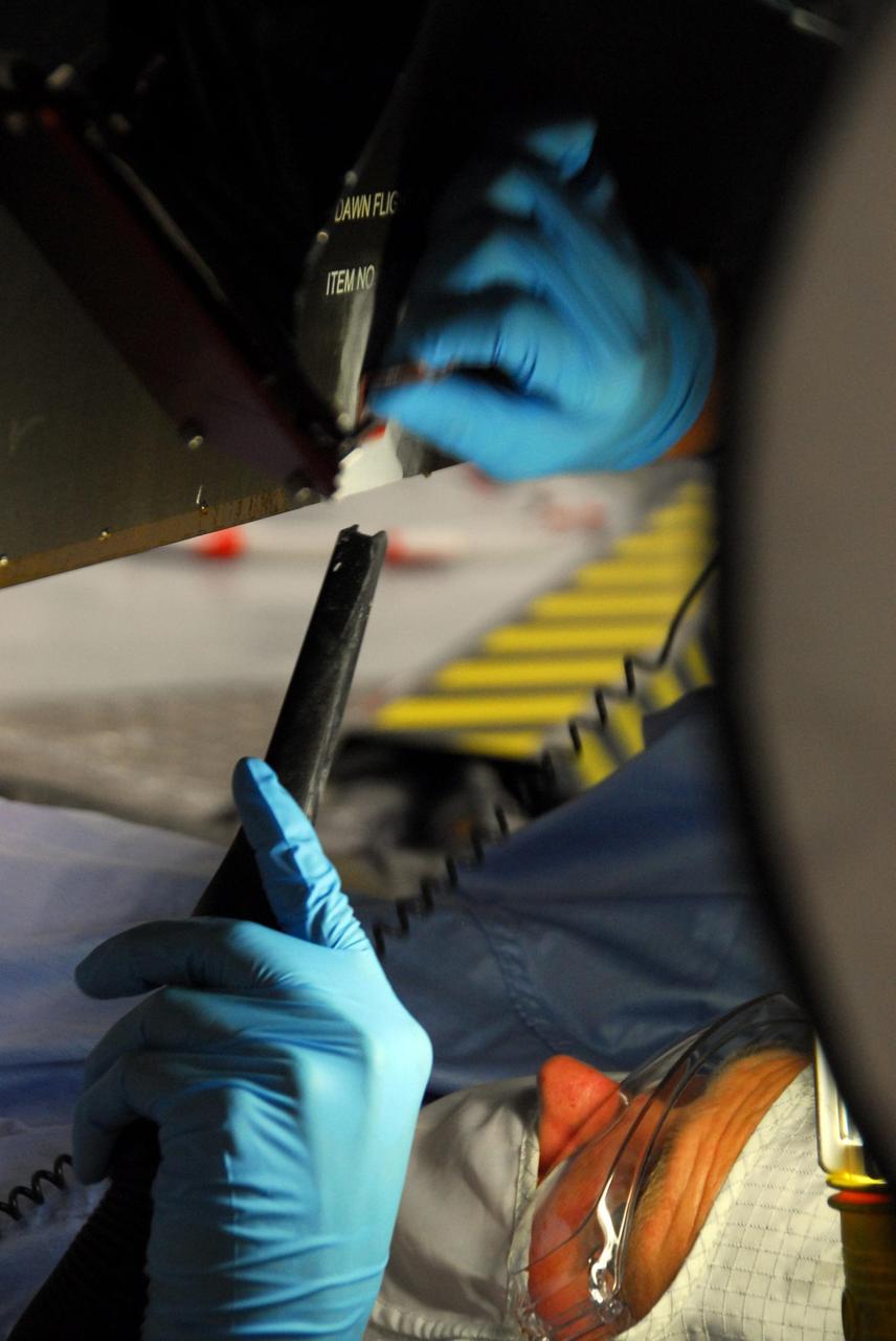 KENNEDY SPACE CENTER, FLA. -- At Astrotech, a Dutch Space technician repairs the damage to the lower edge of the solar array panel on the Dawn spacecraft. On June 11, during a procedure to prepare the Dawn spacecraft for spin-balance testing, the back of a solar array panel was slightly damaged by a technician's tool. The size of the affected area is about 2.5 inches by 2 inches. There is no impact to the launch date of July 7. Dawn's goal is to characterize the conditions and processes of the solar system's earliest epoch 4.5 billion years ago by investigating in detail two of the largest asteroids, Ceres and Vesta. They reside between Mars and Jupiter in the asteroid belt. Photo credit: NASA/George Shelton