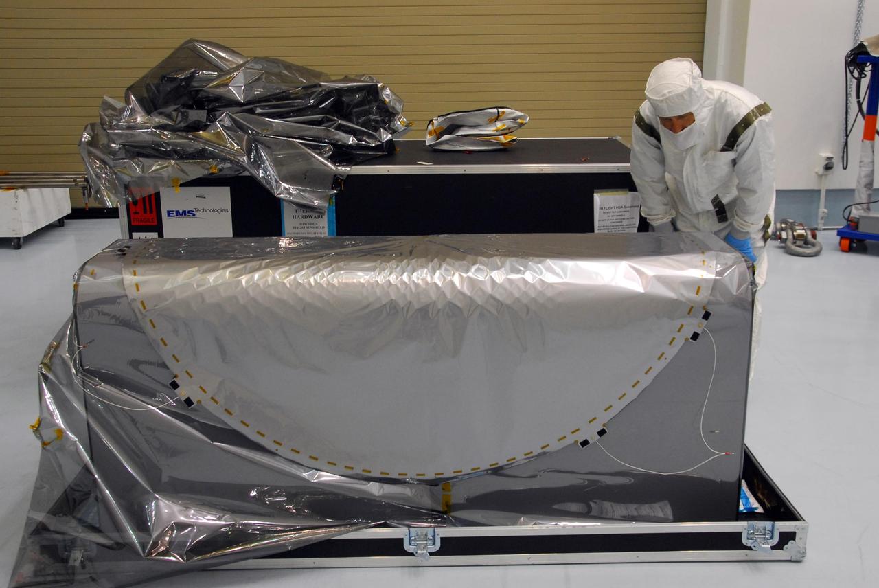 KENNEDY SPACE CENTER, FLA. -- At Astrotech, a technician looks at the sun shade (foreground) to be installed over the high gain antenna on the Dawn spacecraft. Made of germanium kapton, the shade, which is RF transparent, is placed over the sensitive antenna to reflect and emit harmful solar radiation to prevent the antenna from being excessively heated. Dawn is scheduled to launch July 7 from Pad 17-B on Cape Canaveral Air Force Station. Dawn's goal is to characterize the conditions and processes of the solar system's earliest epoch by investigating in detail the largest protoplanets that have remained intact since their formations: asteroid Vesta and the dwarf planet Ceres. They reside in the extensive zone between Mars and Jupiter together with many other smaller bodies, called the asteroid belt. Photo credit: NASA/George Shelton