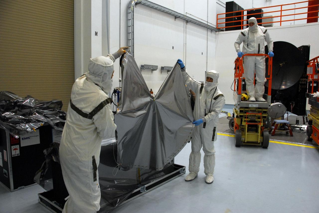 KENNEDY SPACE CENTER, FLA. -- At Astrotech, technicians lift the sun shade to be installed over the high gain antenna on the Dawn spacecraft. Made of germanium kapton, the shade, which is RF transparent, is placed over the sensitive antenna to reflect and emit harmful solar radiation to prevent the antenna from being excessively heated. Dawn is scheduled to launch July 7 from Pad 17-B on Cape Canaveral Air Force Station. Dawn's goal is to characterize the conditions and processes of the solar system's earliest epoch by investigating in detail the largest protoplanets that have remained intact since their formations: asteroid Vesta and the dwarf planet Ceres. They reside in the extensive zone between Mars and Jupiter together with many other smaller bodies, called the asteroid belt. Photo credit: NASA/George Shelton