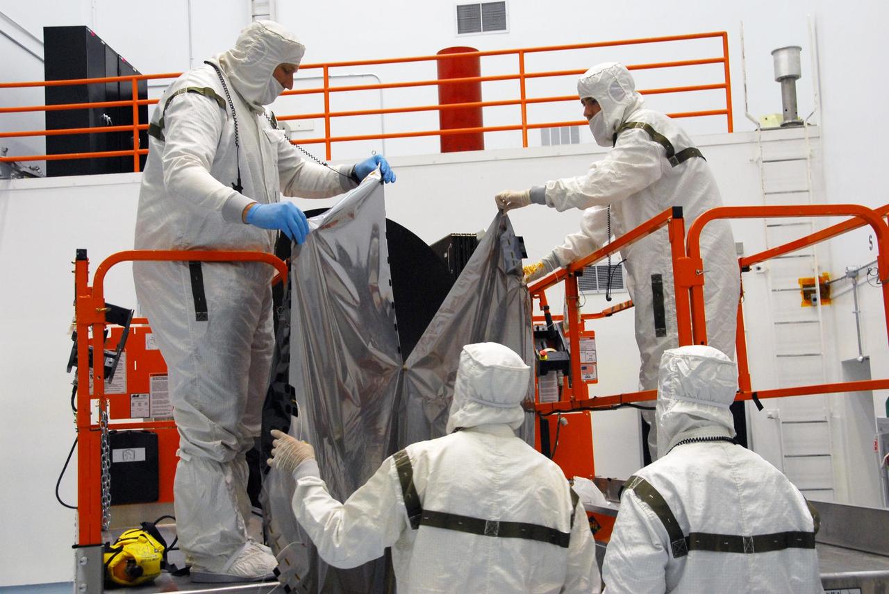 KENNEDY SPACE CENTER, FLA. -- At Astrotech, technicians lift the sun shade toward the Dawn spacecraft to install it on the high gain antenna. Made of germanium kapton, the shade, which is RF transparent, is placed over the sensitive antenna to reflect and emit harmful solar radiation to prevent the antenna from being excessively heated. Dawn is scheduled to launch July 7 from Pad 17-B on Cape Canaveral Air Force Station. Dawn's goal is to characterize the conditions and processes of the solar system's earliest epoch by investigating in detail the largest protoplanets that have remained intact since their formations: asteroid Vesta and the dwarf planet Ceres. They reside in the extensive zone between Mars and Jupiter together with many other smaller bodies, called the asteroid belt. Photo credit: NASA/George Shelton