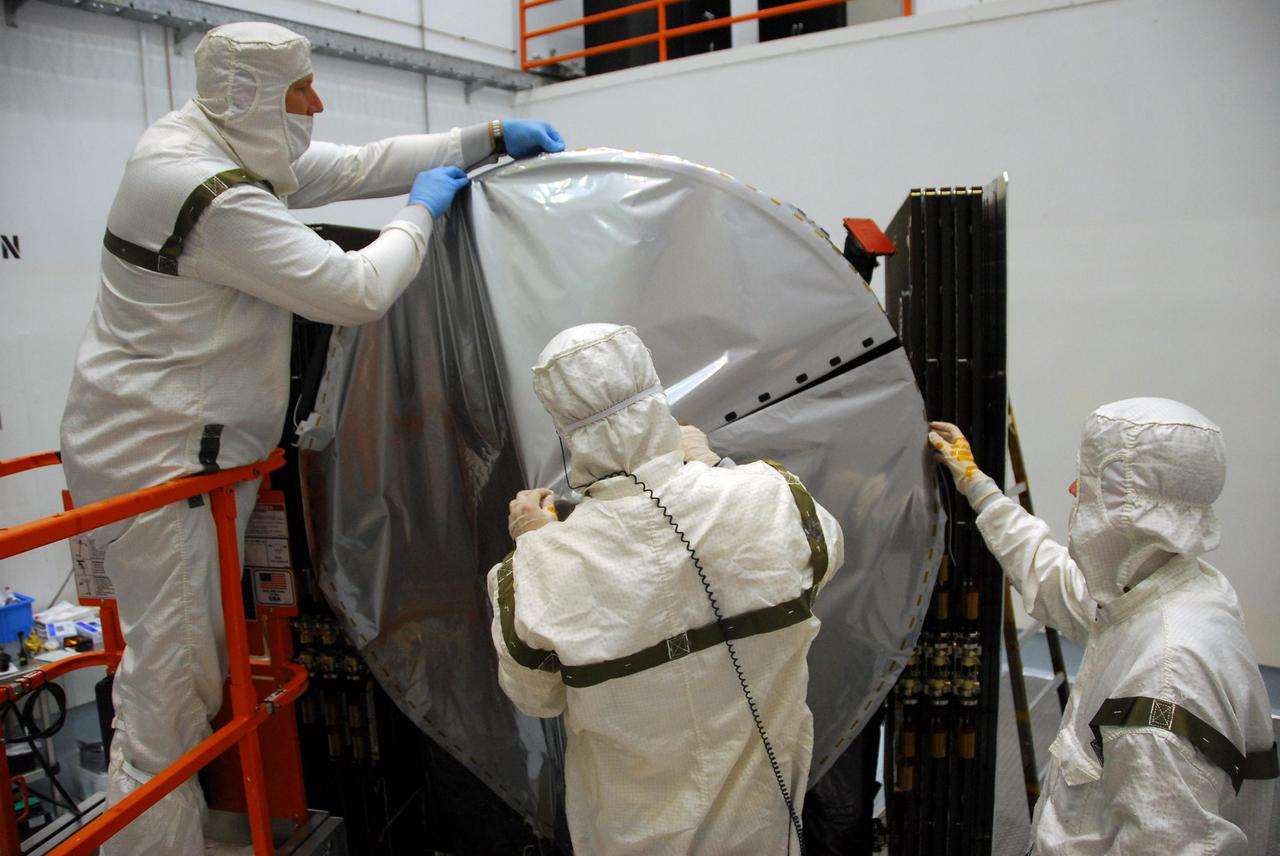 KENNEDY SPACE CENTER, FLA. -- At Astrotech, technicians secure all sides of the sun shade over the high gain antenna on the Dawn spacecraft. Made of germanium kapton, the shade, which is RF transparent, is placed over the sensitive antenna to reflect and emit harmful solar radiation to prevent the antenna from being excessively heated. Dawn is scheduled to launch July 7 from Pad 17-B on Cape Canaveral Air Force Station. Dawn's goal is to characterize the conditions and processes of the solar system's earliest epoch by investigating in detail the largest protoplanets that have remained intact since their formations: asteroid Vesta and the dwarf planet Ceres. They reside in the extensive zone between Mars and Jupiter together with many other smaller bodies, called the asteroid belt. Photo credit: NASA/George Shelton