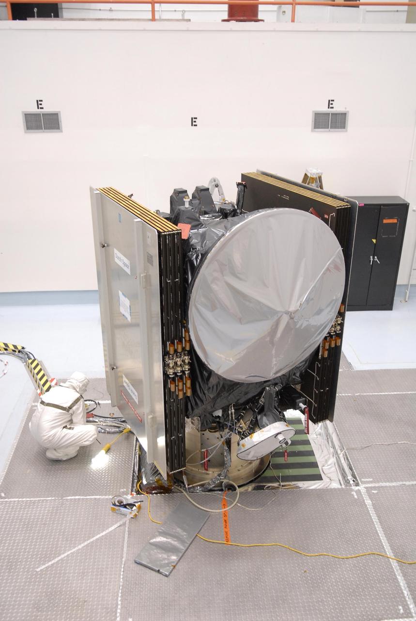 KENNEDY SPACE CENTER, FLA. -- At Astrotech, the Dawn spacecraft is on display for a media showing.  On each side are the folded solar array panels. At the top is the high gain antenna, covered by a sun shade.  At the bottom, also under cover, is one of the ion propulsion thrusters. Behind the antenna on the outside edge are the framing cameras.  Dawn's goal is to characterize the conditions and processes of the solar system's earliest epoch by investigating in detail the largest protoplanets that have remained intact since their formations: asteroid Vesta and the dwarf planet Ceres.  They reside in the extensive zone between Mars and Jupiter together with many other smaller bodies, called the asteroid belt.   Photo credit: NASA/Kim Shiflett