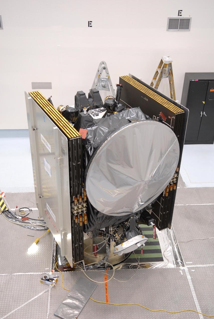 KENNEDY SPACE CENTER, FLA. -- At Astrotech, the Dawn spacecraft is on display for a media showing. On each side are the folded solar array panels. At the top is the high gain antenna, covered by a sun shade. At the bottom, also under cover, is one of the ion propulsion thrusters. Behind the antenna on the outside edge are the framing cameras, which are the scientific imaging system of the Dawn Mission. Dawn's goal is to characterize the conditions and processes of the solar system's earliest epoch by investigating in detail the largest protoplanets that have remained intact since their formations: asteroid Vesta and the dwarf planet Ceres. They reside in the extensive zone between Mars and Jupiter together with many other smaller bodies, called the asteroid belt. Photo credit: NASA/Kim Shiflett
