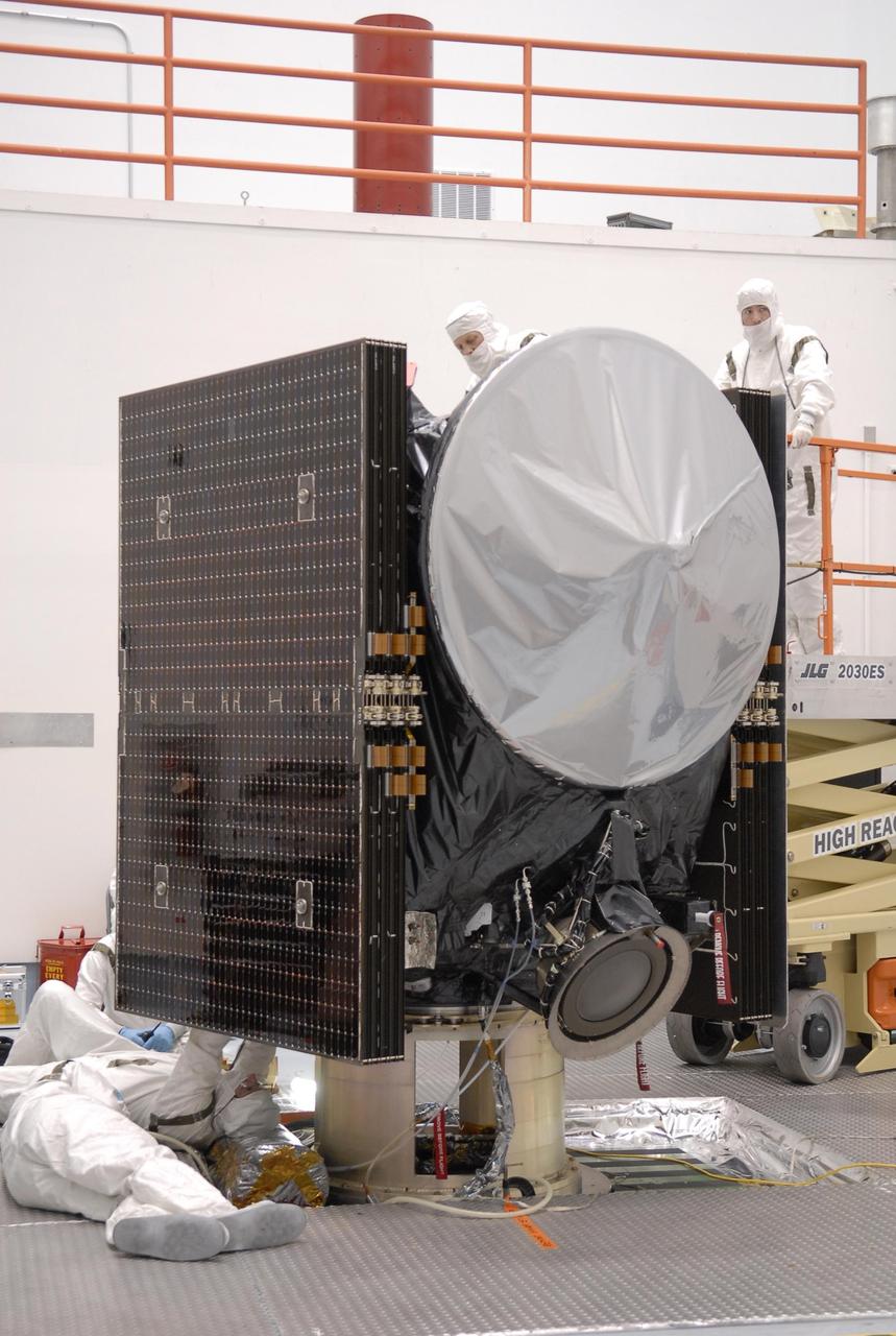 KENNEDY SPACE CENTER, FLA. -- At Astrotech, technicians prepare the Dawn spacecraft for a media showing. On each side are the folded solar array panels. At the top is the high gain antenna, covered by a sun shade. At the bottom is one of the ion propulsion thrusters. Dawn's goal is to characterize the conditions and processes of the solar system's earliest epoch by investigating in detail the largest protoplanets that have remained intact since their formations: asteroid Vesta and the dwarf planet Ceres. They reside in the extensive zone between Mars and Jupiter together with many other smaller bodies, called the asteroid belt. Photo credit: NASA/Kim Shiflett