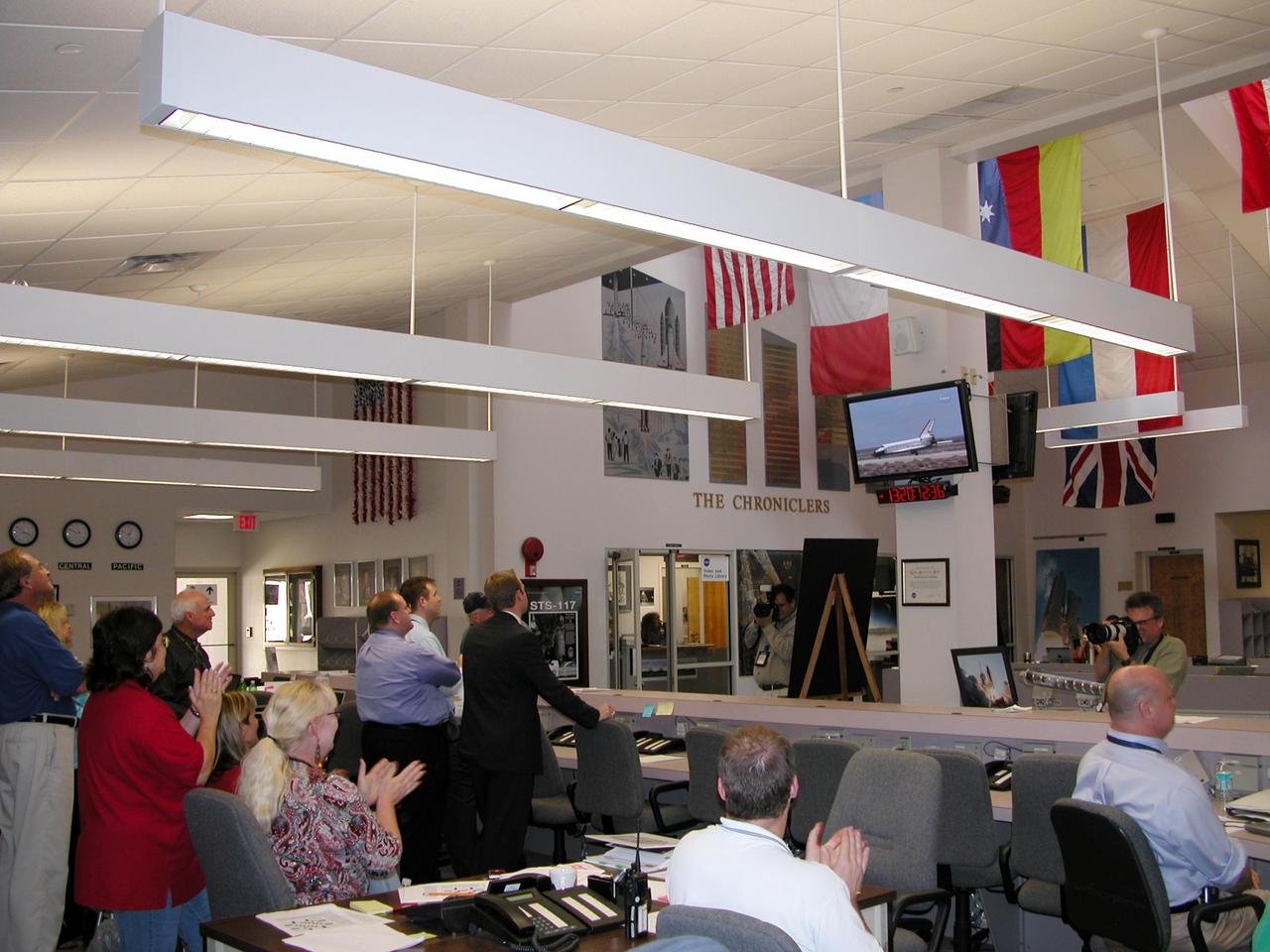 KENNEDY SPACE CENTER, FLA. -- Media and staff in the NASA News Center at Kennedy Space Center applaud the successful landing of Atlantis, visible on the television screens, at NASA's Dryden Flight Research Center at Edwards Air Force Base in California. Returning from mission STS-117, Atlantis touched down on runway 22 at Edwards on orbit 219 after 13 days, 20 hours and 12 minutes in space.  The landing was diverted to California due to marginal weather at the Kennedy Space Center.  Main gear touchdown was at 3:49:38 p.m. EDT on runway 22.  Nose gear touchdown was at 3:49:49 p.m. and wheel stop was at 3:50:48 p.m.  This was the 51st landing for the Space Shuttle Program at Edwards Air Force Base. The mission to the International Space Station was a success, installing the S3/S4 truss.  The returning crew of seven includes astronaut Sunita Williams, who was flight engineer on the Expedition 15 crew.  She achieved a new milestone, a record-setting flight at 194 days, 18 hours and 58 minutes, the longest single spaceflight ever by a female astronaut or cosmonaut.  Photo credit: NASA/Debbie Odom