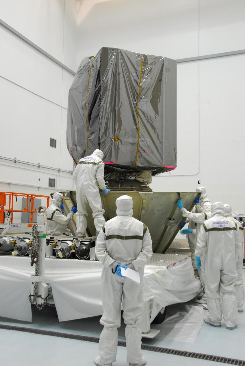 KENNEDY SPACE CENTER, FLA. --     At Astrotech, technicians place another segment of the canister around the upper stage booster below the Dawn spacecraft.  When enclosed in the canister, Dawn will be transported to Launch Pad 17-B and lifted into the mobile service tower for mating with the Delta II launch vehicle. The Delta II-Heavy, manufactured by the United Launch Alliance, is scheduled to launch the Dawn spacecraft on its 4-year flight to the asteroid belt.  The Delta II-Heavy will use three stages and nine solid-fueled booster rockets to propel Dawn on its way. A 9.5-foot payload fairing will protect the spacecraft from the heat and stresses of launch. Dawn's goal is to characterize the conditions and processes of the solar system's earliest epoch by investigating in detail the largest protoplanets that have remained intact since their formations: asteroid Vesta and the dwarf planet Ceres.  They reside in the extensive zone between Mars and Jupiter together with many other smaller bodies, called the asteroid belt.  Dawn is scheduled to launch July 7.    Photo credit: NASA/George Shelton