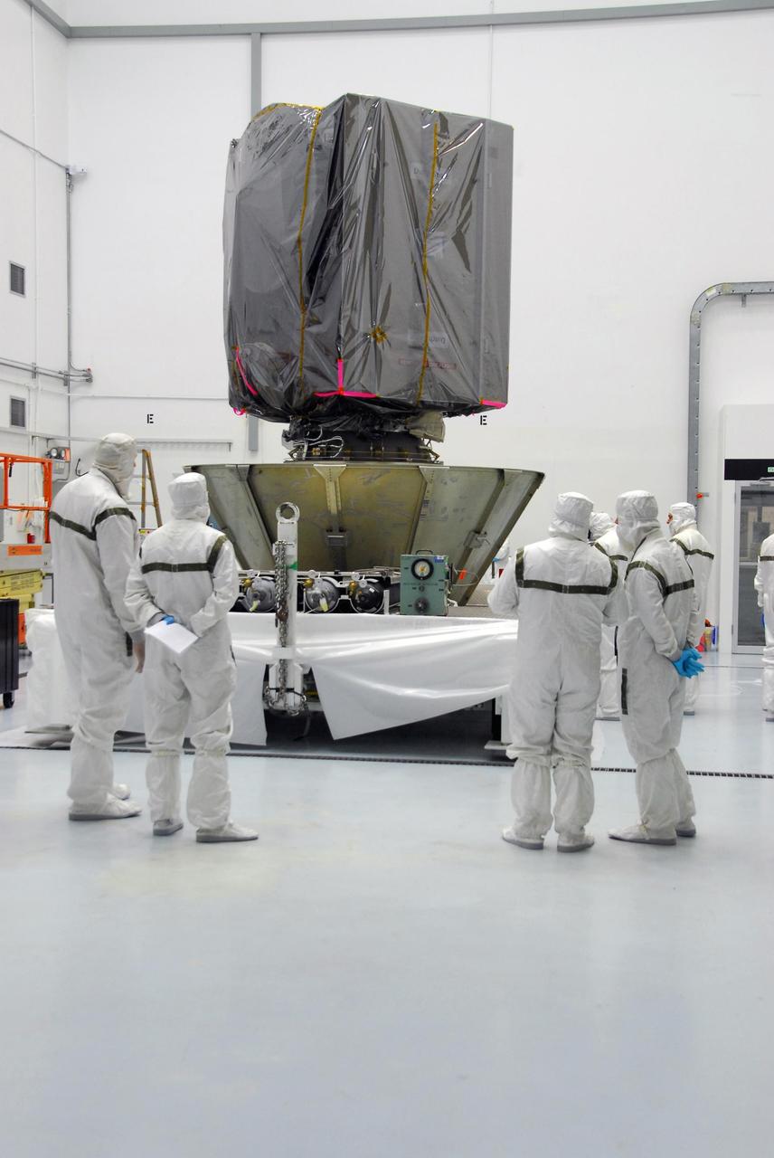KENNEDY SPACE CENTER, FLA. --     At Astrotech, technicians examine the lower canister they placed around the bottom of the Dawn spacecraft.  When enclosed in the canister, Dawn will be transported to Launch Pad 17-B and lifted into the mobile service tower for mating with the Delta II launch vehicle. The Delta II-Heavy, manufactured by the United Launch Alliance, is scheduled to launch the Dawn spacecraft on its 4-year flight to the asteroid belt.  The Delta II-Heavy will use three stages and nine solid-fueled booster rockets to propel Dawn on its way. A 9.5-foot payload fairing will protect the spacecraft from the heat and stresses of launch. Dawn's goal is to characterize the conditions and processes of the solar system's earliest epoch by investigating in detail the largest protoplanets that have remained intact since their formations: asteroid Vesta and the dwarf planet Ceres.  They reside in the extensive zone between Mars and Jupiter together with many other smaller bodies, called the asteroid belt.  Dawn is scheduled to launch July 7.    Photo credit: NASA/George Shelton