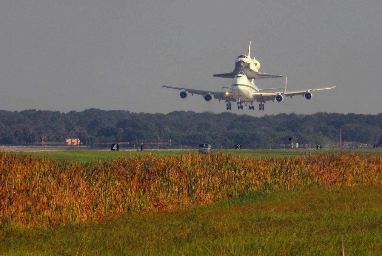 KENNEDY SPACE CENTER, FLA. -- The shuttle carrier aircraft, or SCA, and its piggyback passenger Atlantis approach the runway at the KSC Shuttle Landing Facility after a three-day trip from California. Touchdown was at 8:27 a.m. EDT. The SCA is a modified Boeing 747 jetliner. Atlantis landed at Edwards Air Force Base in California to end mission STS-117. The return to KSC began July 1 and took three days after stops across the country for fuel. The last stop was at Ft. Campbell in Kentucky. Weather conditions over the last leg postponed the return trip until July 3. Atlantis will be removed from the back of the SCA via the mate/demate device at the SLF. It will then be towed to the Orbiter Processing Facility to begin processing for its next launch, mission STS-122 in December. Photo credit: NASA/George Shelton