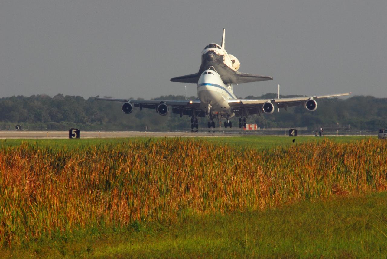 KENNEDY SPACE CENTER, FLA. -- The shuttle carrier aircraft, or SCA, and its piggyback passenger Atlantis near touchdown on the runway at the KSC Shuttle Landing Facility after a three-day trip from California. Touchdown was at 8:27 a.m. EDT. The SCA is a modified Boeing 747 jetliner. Atlantis landed at Edwards Air Force Base in California to end mission STS-117. The return to KSC began July 1 and took three days after stops across the country for fuel. The last stop was at Ft. Campbell in Kentucky. Weather conditions over the last leg postponed the return trip until July 3. Atlantis will be removed from the back of the SCA via the mate/demate device at the SLF. It will then be towed to the Orbiter Processing Facility to begin processing for its next launch, mission STS-122 in December. Photo credit: NASA/George Shelton