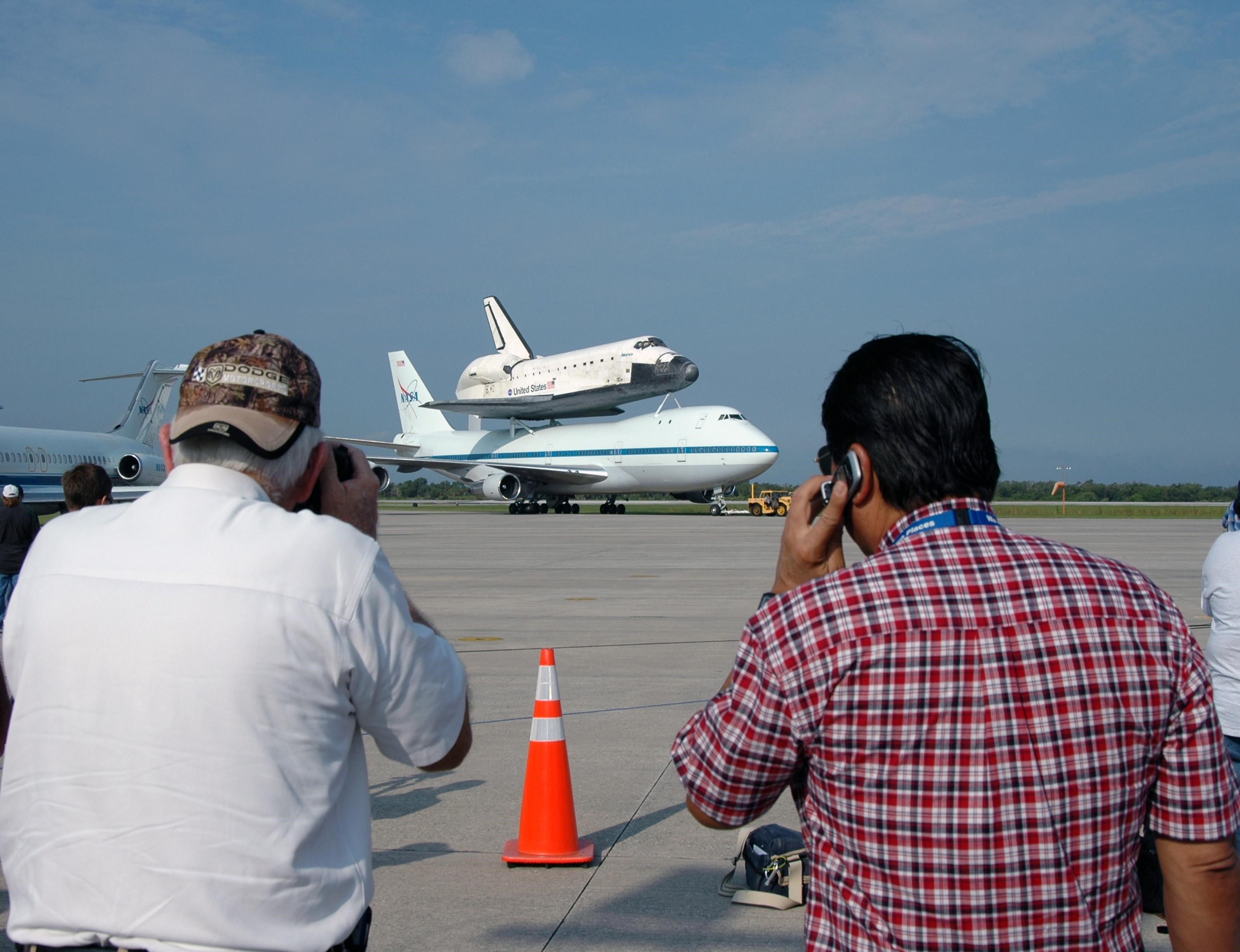 KENNEDY SPACE CENTER, FLA. -- Media are gathered at the KSC Shuttle Landing Facility to watch the arrival of the orbiter Atlantis on the back of the shuttle carrier aircraft, or SCA. Touchdown was at 8:27 a.m. EDT. The SCA is a modified Boeing 747 jetliner. Atlantis landed at Edwards Air Force Base in California to end mission STS-117. The return to KSC began July 1 and took three days after stops across the country for fuel. The last stop was at Ft. Campbell in Kentucky. Weather conditions over the last leg postponed the return trip until July 3. Atlantis will be removed from the back of the SCA via the mate/demate device at the SLF. It will then be towed to the Orbiter Processing Facility to begin processing for its next launch, mission STS-122 in December. Photo credit: NASA/Jim Grossmann