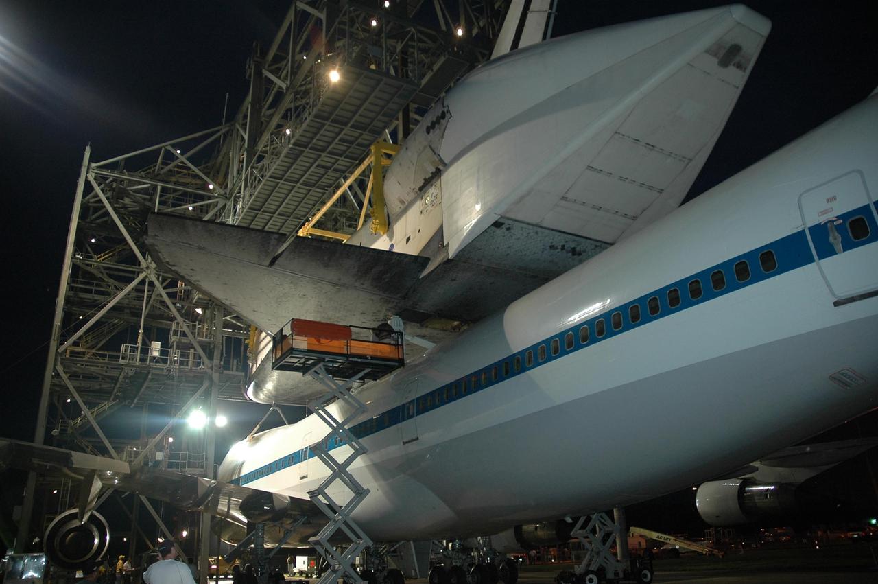 KENNEDY SPACE CENTER, FLA. -- At the mate/demate device at Kennedy Space Center's Shuttle Landing Facility, the lifting crane begins to lift Atlantis up from the shuttle carrier aircraft, or SCA, beneath it. Visible on Atlantis is the tail cone that covers and protects the main engines during the ferry flight. Technicians monitor the lifting process on a raised platform to the left. Atlantis arrived at Kennedy Space Center atop the SCA on July 3 after a three-day, cross-country flight due to fuel stops and weather delays. Touchdown was at 8:27 a.m. EDT. Atlantis landed at Edwards Air Force Base in California on June 22 to end mission STS-117. Photo credit: NASA/Jack Pfaller.