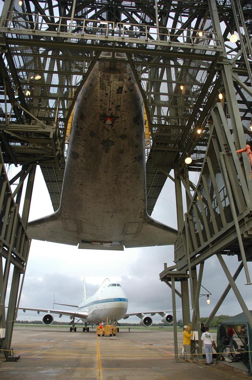 KENNEDY SPACE CENTER, FLA. -- At the mate/demate device at Kennedy Space Center's Shuttle Landing Facility, work begins to lower Atlantis to the ground. In the background, a towing device is used to back the shuttle carrier aircraft, or SCA, away from the device. When the orbiter is lowered to the ground it will be towed to the Orbiter Processing Facility to begin processing for its next launch, mission STS-122 in December. Atlantis arrived at Kennedy Space Center atop the SCA on July 3 after a three-day, cross-country flight due to fuel stops and weather delays. Touchdown was at 8:27 a.m. EDT. Atlantis landed at Edwards Air Force Base in California on June 22 to end mission STS-117. Photo credit: NASA/Jack Pfaller.