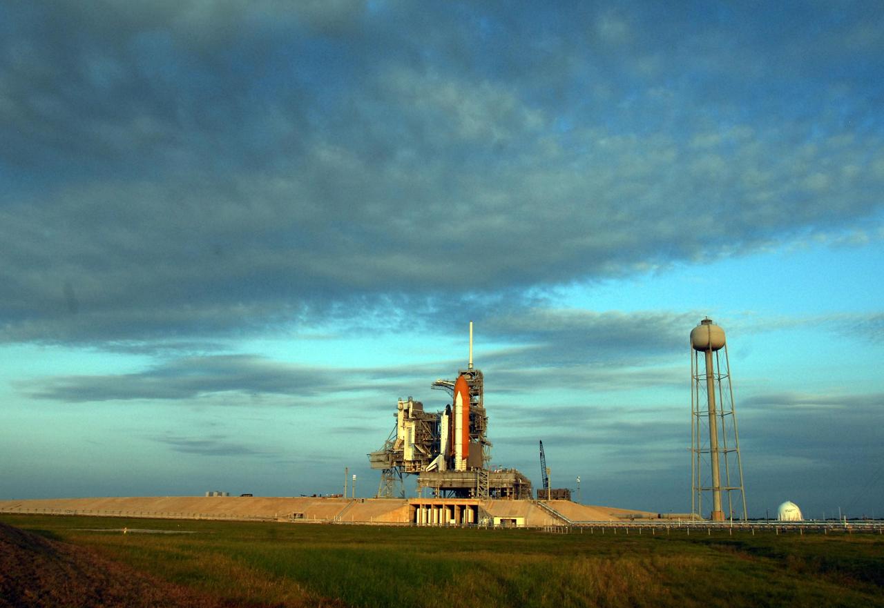 KENNEDY SPACE CENTER, FLA. - Under a sky brushed with gray clouds sits Space Shuttle Endeavour on Launch Pad 39A. Behind the shuttle are the rotating service structure, which can be rolled around to enclose the shuttle for access during processing, and the fixed service structure, topped by an 80-foot-tall lightning mast. At right is the 290-foot-tall water tank, which provides the deluge over the mobile launcher platform for sound suppression during liftoff. Endeavour is scheduled to launch on mission STS-118 on Aug. 7. During the mission, Endeavour will carry into orbit the S5 truss, SPACEHAB module and external stowage platform 3. The mission is the 22nd flight to the International Space Station and will mark the first flight of Mission Specialist Barbara Morgan, the teacher-turned-astronaut whose association with NASA began more than 20 years ago. STS-118 will be the first flight since 2002 for Endeavour, which has undergone extensive modifications, including the addition of safety upgrades already added to orbiters Discovery and Atlantis. Photo credit: NASA/Ken Thornsley