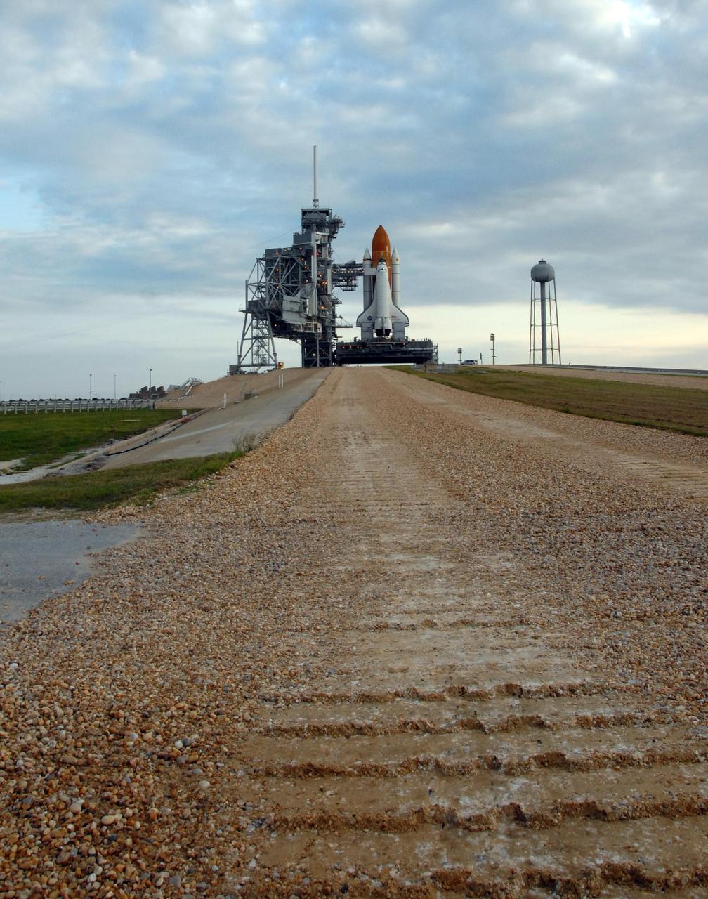 KENNEDY SPACE CENTER, FLA. - The crawler way, in the foreground, still bears the tracks of the crawler-transporter that delivered Space Shuttle Endeavour to Launch Pad 39A, in the background. At far left is the rotating service structure, which can be rolled around to enclose the shuttle for access during processing. Behind it is the fixed service structure, topped by an 80-foot-tall lightning mast. At right is the 290-foot-tall water tank, which provides the deluge over the mobile launcher platform for sound suppression during liftoff. Endeavour is scheduled to launch on mission STS-118 on Aug. 7. During the mission, Endeavour will carry into orbit the S5 truss, SPACEHAB module and external stowage platform 3. The mission is the 22nd flight to the International Space Station and will mark the first flight of Mission Specialist Barbara Morgan, the teacher-turned-astronaut whose association with NASA began more than 20 years ago. STS-118 will be the first flight since 2002 for Endeavour, which has undergone extensive modifications, including the addition of safety upgrades already added to orbiters Discovery and Atlantis. Photo credit: NASA/Ken Thornsley