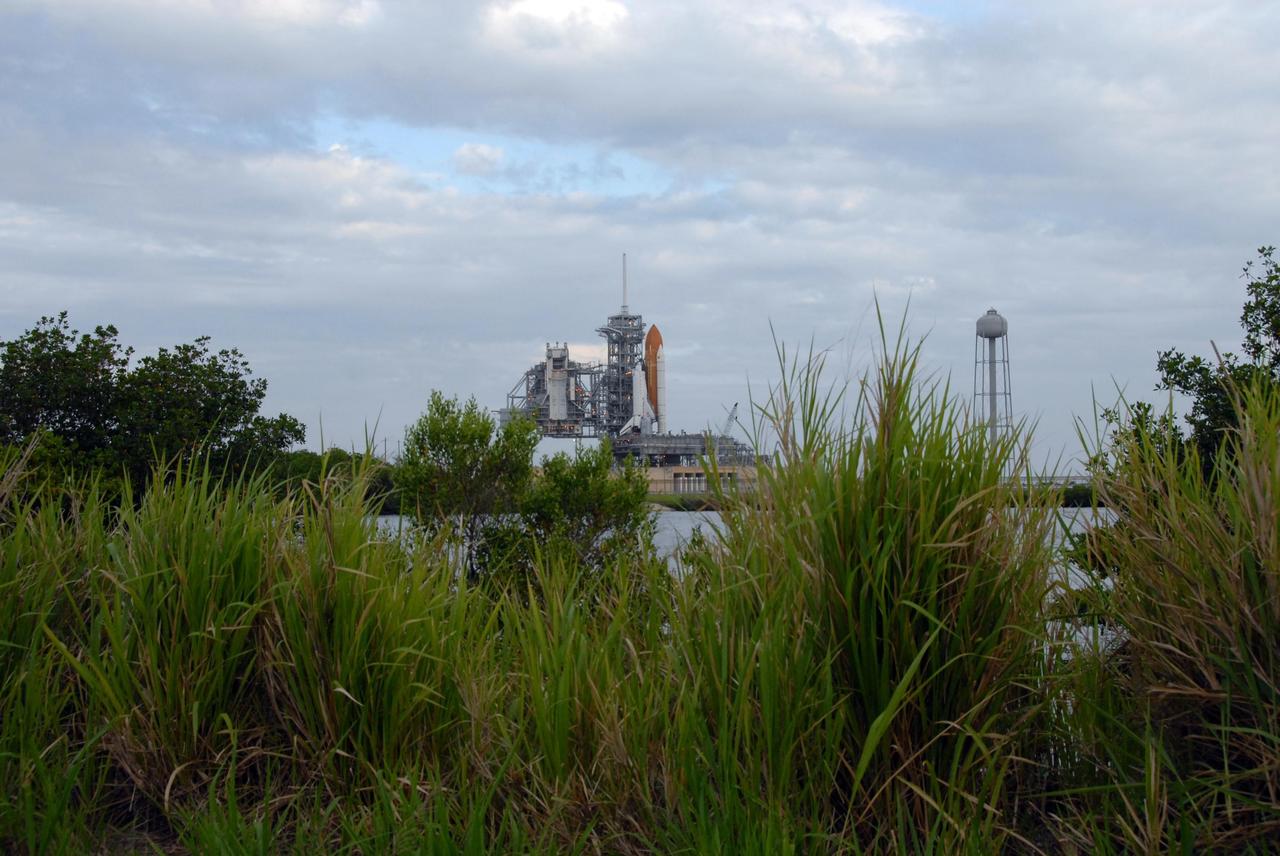 KENNEDY SPACE CENTER, FLA. - Sandwiched between gray clouds and the Banana Creek can be seen Space Shuttle Endeavour on Launch Pad 39A. The shuttle rolled to the pad overnight to get ready for liftoff on mission STS-118. First motion out of the Vehicle Assembly Building was at 8:10 p.m. July 10, and the shuttle was hard down on the pad at 3:02 a.m. July 11. At far left is the rotating service structure, which can be rolled around to enclose the shuttle for access during processing. At right is the 290-foot-tall water tank, which provides the deluge over the mobile launcher platform for sound suppression during liftoff. The proximity of the water and brush and grass signify the close relationship of Kennedy Space Center and the Merritt Island National Wildlife Center, which surrounds it. Endeavour is scheduled to launch on mission STS-118 on Aug. 7. During the mission, Endeavour will carry into orbit the S5 truss, SPACEHAB module and external stowage platform 3. The mission is the 22nd flight to the International Space Station and will mark the first flight of Mission Specialist Barbara Morgan, the teacher-turned-astronaut whose association with NASA began more than 20 years ago. STS-118 will be the first flight since 2002 for Endeavour, which has undergone extensive modifications, including the addition of safety upgrades already added to orbiters Discovery and Atlantis. Photo credit: NASA/Ken Thornsley