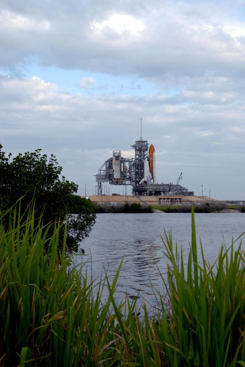 KENNEDY SPACE CENTER, FLA. - Sandwiched between gray clouds and the Banana Creek can be seen Space Shuttle Endeavour on Launch Pad 39A. The shuttle rolled to the pad overnight to get ready for liftoff on mission STS-118. First motion out of the Vehicle Assembly Building was at 8:10 p.m. July 10, and the shuttle was hard down on the pad at 3:02 a.m. July 11. At far left is the rotating service structure, which can be rolled around to enclose the shuttle for access during processing. The proximity of the water and brush and grass signify the close relationship of Kennedy Space Center and the Merritt Island National Wildlife Center, which surrounds it. Endeavour is scheduled to launch on mission STS-118 on Aug. 7. During the mission, Endeavour will carry into orbit the S5 truss, SPACEHAB module and external stowage platform 3. The mission is the 22nd flight to the International Space Station and will mark the first flight of Mission Specialist Barbara Morgan, the teacher-turned-astronaut whose association with NASA began more than 20 years ago. STS-118 will be the first flight since 2002 for Endeavour, which has undergone extensive modifications, including the addition of safety upgrades already added to orbiters Discovery and Atlantis. Photo credit: NASA/Ken Thornsley