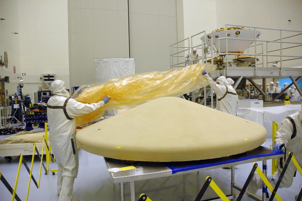 KENNEDY SPACE CENTER, Fla. -- In the Payload Hazardous Servicing Facility, workers remove the covering over the heat shield (foreground) for the Phoenix Mars Lander spacecraft before installation. Targeted for launch from Cape Canaveral Air Force Station on Aug. 3, Phoenix will land in icy soils near the north polar permanent ice cap of Mars and explore the history of the water in these soils and any associated rocks, while monitoring polar climate. Landing on Mars is planned in May 2008 on arctic ground where a mission currently in orbit, Mars Odyssey, has detected high concentrations of ice just beneath the top layer of soil. Photo credit: NASA/Troy Cryder