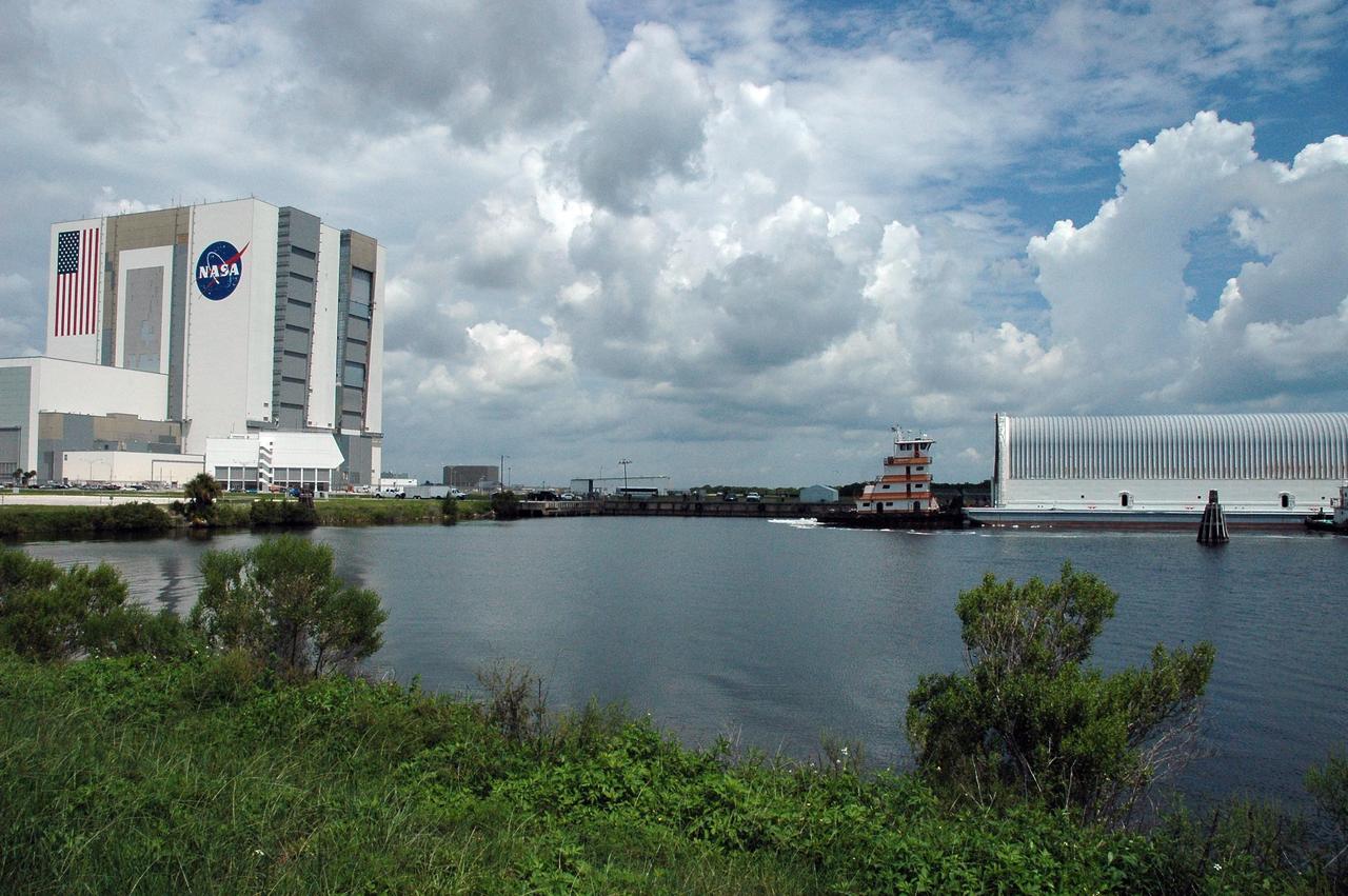 KENNEDY SPACE CENTER, FLA. --   The Pegasus barge, at right, is towed toward the landing dock in the Launch Complex 39 Area.  The barge carries external tank No. 120, to be used for launching Space Shuttle Discovery on mission STS-120 in October.  At left is the Vehicle Assembly Building. The barge has carried the tank from the Michoud Assembly Facility near New Orleans, making the journey around the Florida peninsula in tow by the JA Bisso II  tugboat, to Port Canaveral and Kennedy Space Center. After the tank is offloaded, it will be towed to the Vehicle Assembly Building for lifting into a checkout cell.   NASA/Amanda Diller