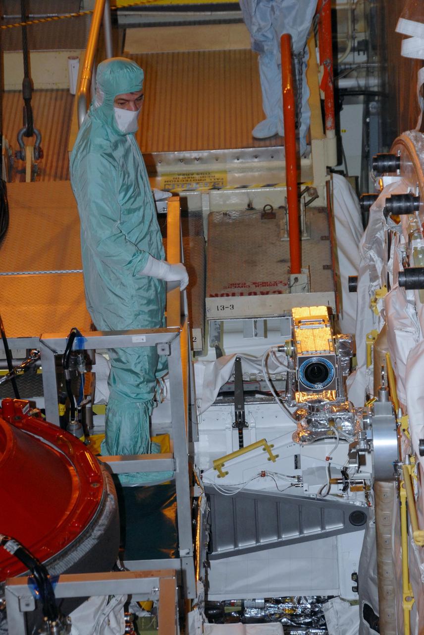 KENNEDY SPACE CENTER, FLA. - In Orbiter Processing Facility bay 3, STS-120 crew members get a close look at hardware in Discovery's payload bay.  In the bucket at left is Mission Specialist Paolo A. Nespoli, who is a European Space Agency astronaut from Italy.  The object with the  shiny gold surface is a payload bay bulkhead camera.  The STS-120 crew is at Kennedy for a crew equipment interface test, or CEIT, which includes harness training, inspection of the thermal protection system and camera operation for planned extravehicular activities, or EVAs. The STS-120 mission will deliver the Harmony module, christened after a school contest, which will provide attachment points for European and Japanese laboratory modules on the International Space Station. Known in technical circles as Node 2, it is similar to the six-sided Unity module that links the U.S. and Russian sections of the station. Built in Italy for the United States, Harmony will be the first new U.S. pressurized component to be added.  The STS-120 mission is targeted to launch on Oct. 20.  Photo credit: NASA/George Shelton