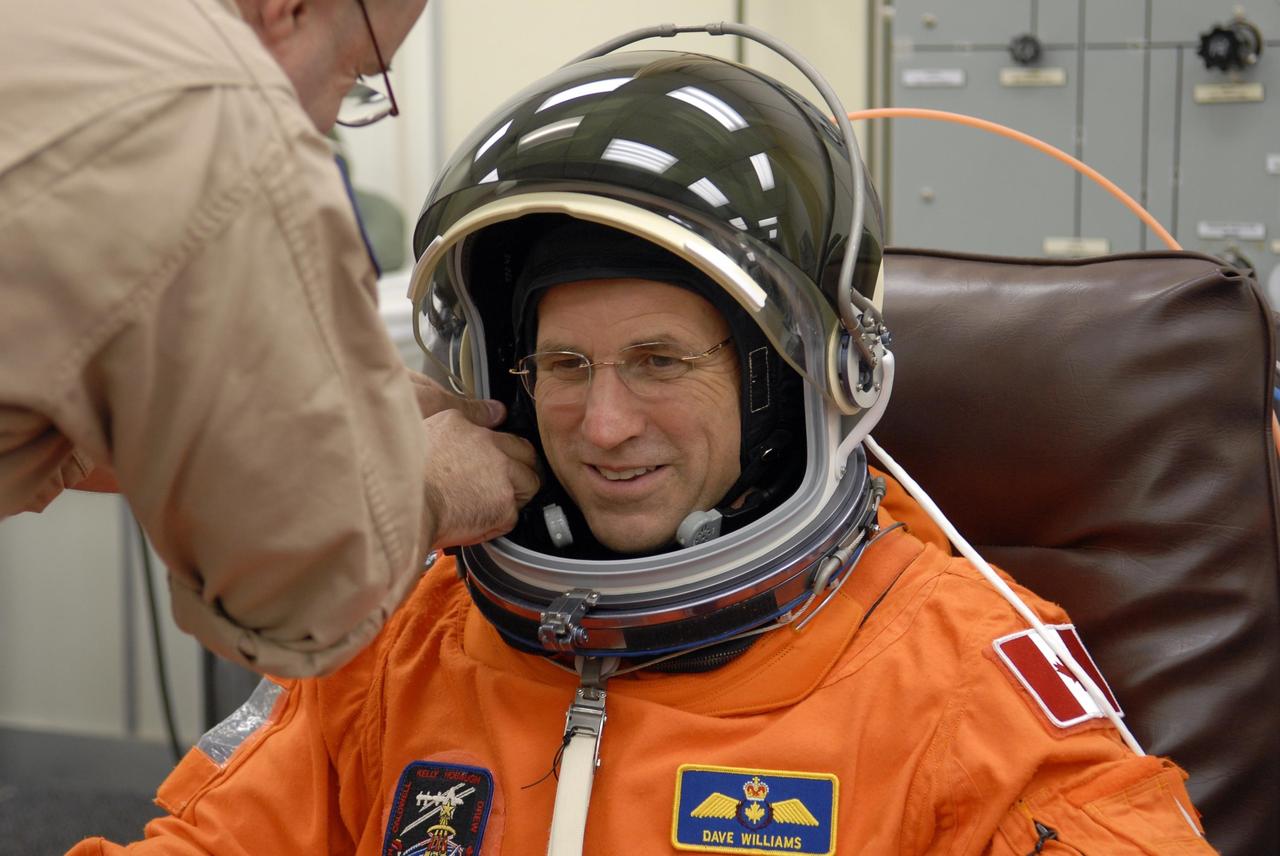 KENNEDY SPACE CENTER, FLA. -- In the Operations and Checkout Building, STS-118 Mission Specialist Dave Williams is helped adjusting his helmet as he suits up for launch.  Williams, who is making his second spaceflight, represents the Canadian Space Agency. Space Shuttle Endeavour's STS-118 mission is the 22nd shuttle flight to the International Space Station. It will continue space station construction by delivering a third starboard truss segment, S5, and other payloads such as the SPACEHAB module and the external stowage platform 3.  The 11-day mission may be extended to as many as 14 depending on the test of the Station-to-Shuttle Power Transfer System that will allow the docked shuttle to draw electrical power from the station and extend its visits to the orbiting lab.  NASA/Kim Shiflett
