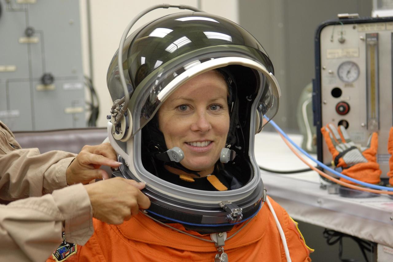 KENNEDY SPACE CENTER, FLA. --  In the Operations and Checkout Building, STS-118 Mission Specialist Tracy Caldwell is helped with her helmet during suitup for launch on Space Shuttle Endeavour. The STS-118 mission is the 22nd shuttle flight to the International Space Station. It will continue space station construction by delivering a third starboard truss segment, S5, and other payloads such as the SPACEHAB module and the external stowage platform 3.  The 11-day mission may be extended to as many as 14 depending on the test of the Station-to-Shuttle Power Transfer System that will allow the docked shuttle to draw electrical power from the station and extend its visits to the orbiting lab.  NASA/Kim Shiflett