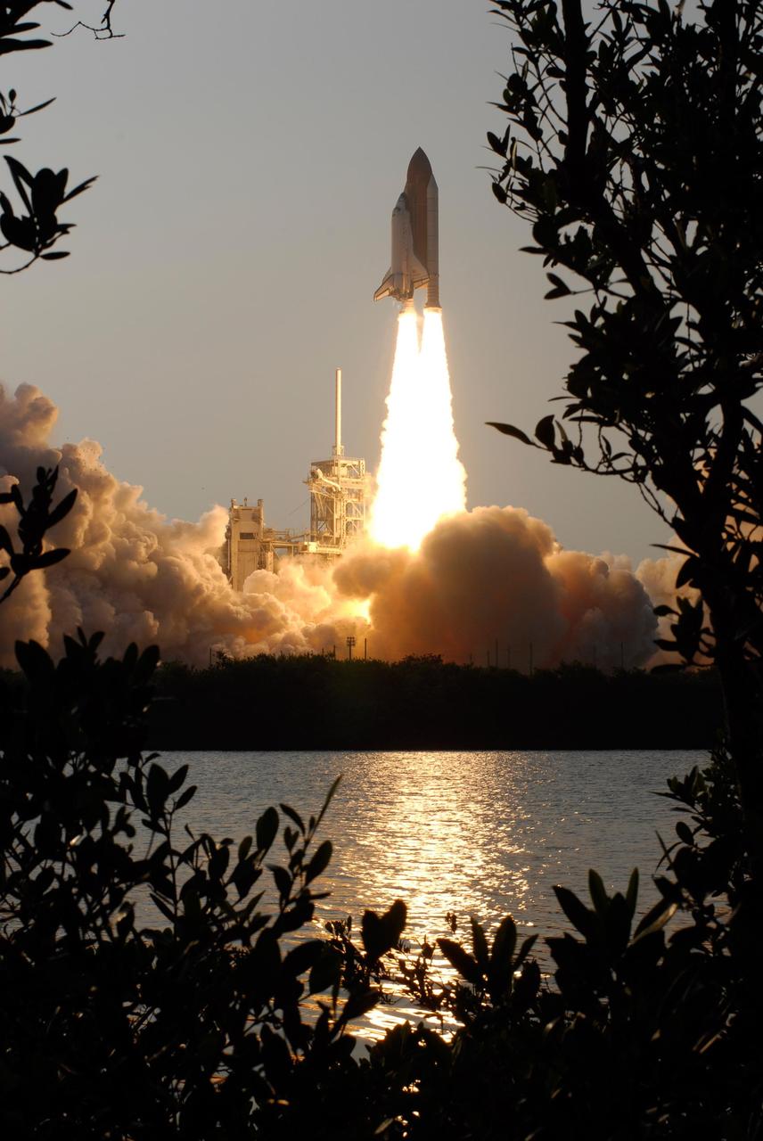 KENNEDY SPACE CENTER, FLA. -- Framed by the trees across the water, Space Shuttle Endeavour clears the lightning mast on Launch Pad 39A as it roars into the sky on mission STS-118. Liftoff of Endeavour was on time at 6:36 p.m. EDT.  The mission is the 22nd shuttle flight to the International Space Station. It will continue space station construction by delivering a third starboard truss segment, S5, and other payloads such as the SPACEHAB module and the external stowage platform 3.  The 11-day mission may be extended to as many as 14 depending on the test of the Station-to-Shuttle Power Transfer System that will allow the docked shuttle to draw electrical power from the station and extend its visits to the orbiting lab.  Photo credit: NASA/Sandra Joseph, Tony Gray, Robert Murray