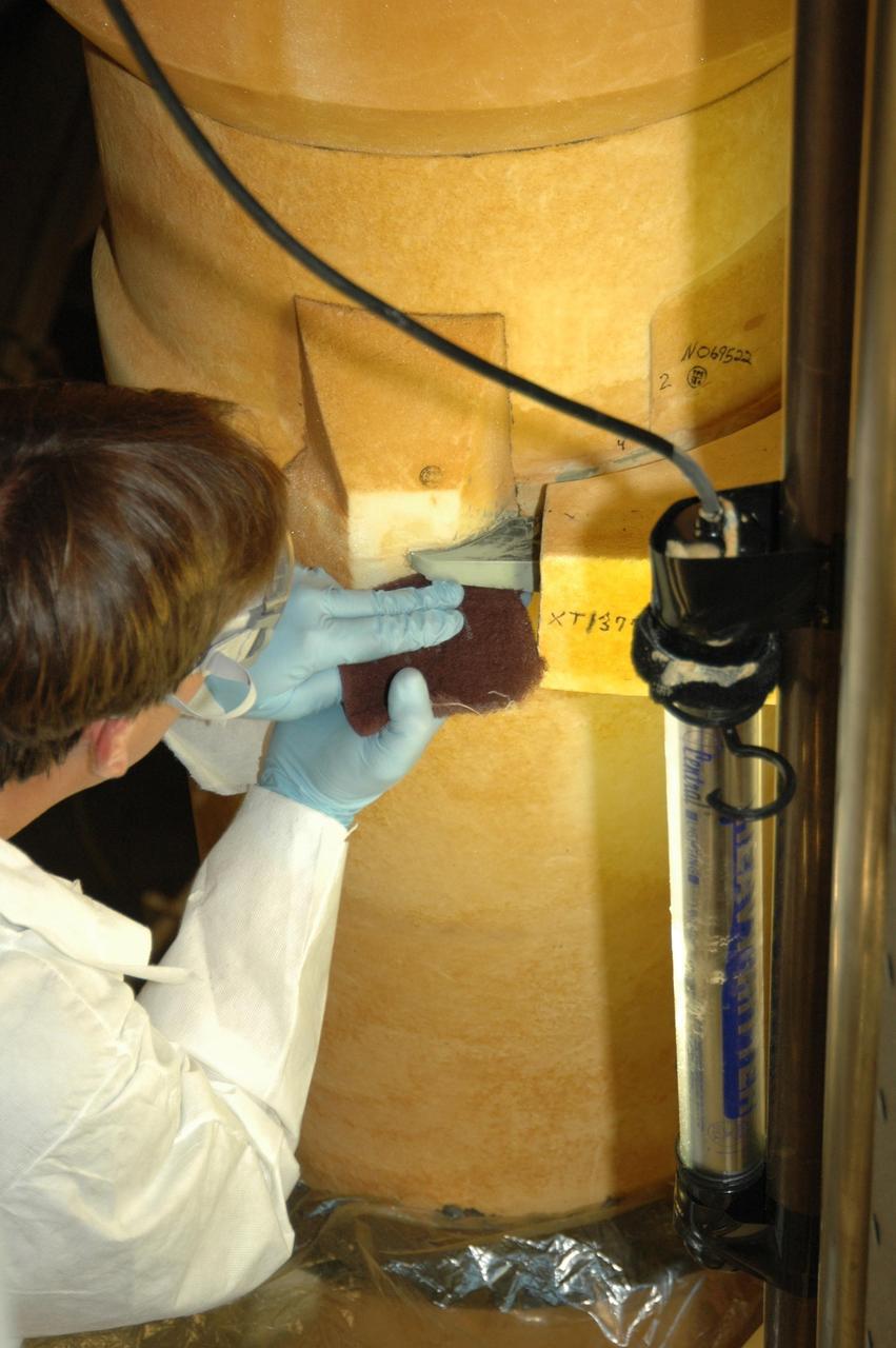 KENNEDY SPACE CENTER, FLA. -- The super lightweight ablator, or SLA, cork insulation has been removed from the external tank and a United Space Alliance external tank technician sands off the residue from the LO2 feed line bracket. The BX265 foam insulation will later be reapplied without the SLA.  The tank is scheduled to fly on Space Shuttle Discovery in October 2007 on mission STS-120.  Discovery's crew will add the module Harmony that will serve as a port for installing additional international laboratories. Harmony will be the first expansion of the living and working space on the complex since the Russian Pirs airlock was installed in 2001. The mission also will move the first set of solar arrays installed on the station to a permanent location on the complex and redeploy them.  Photo credit: NASA/Jim Grossmann