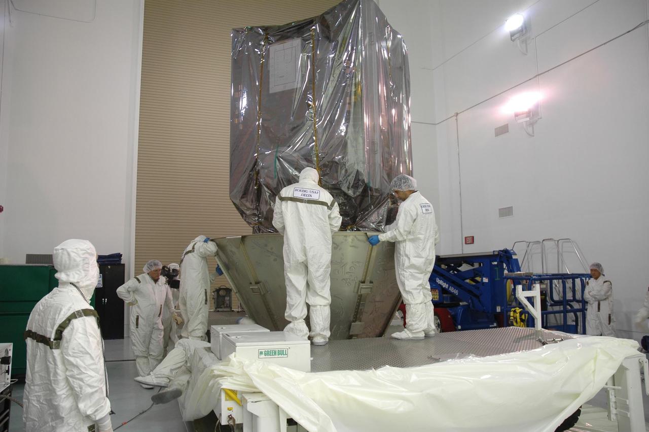 KENNEDY SPACE CENTER, FLA. -- At Astrotech Space Operations in Titusville, Fla., workers place the lower segments of the transportation canister around the upper stage booster beneath the Dawn spacecraft.  The canister will protect the spacecraft and booster during transfer to Launch Pad 17-B at Cape Canaveral Air Force Station (CCAFS). During its nearly decade-long mission, the Dawn mission will study the asteroid Vesta and dwarf planet Ceres, celestial bodies believed to have accreted early in the history of the solar system. To carry out its scientific mission, the Dawn spacecraft will carry a visible camera, a visible and infrared mapping spectrometer, and a gamma ray and neutron spectrometer, whose data will be used in combination to characterize these bodies.  In addition to the three instruments, radiometric and optical navigation data will provide data relating to the gravity field and thus bulk properties and internal structure of the two bodies. Data returned from the Dawn spacecraft could provide opportunities for significant breakthroughs in our knowledge of how the solar system formed. Launch via a Delta II rocket is scheduled in a window from 7:25 to 7:54 a.m. Sept. 26 from CCAFS.  Photo credit: NASA/Jim Grossmann