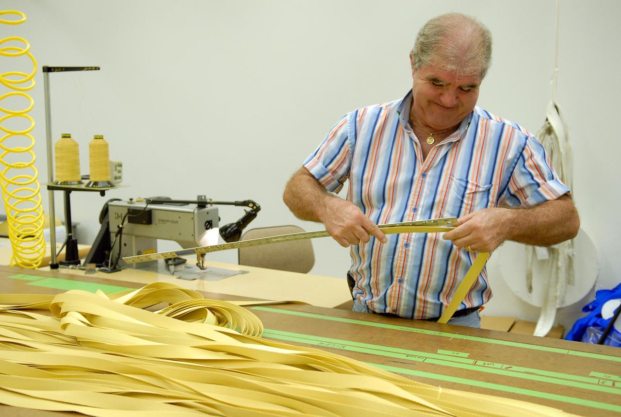 KENNEDY SPACE CENTER, FLA. -- A worker measures straps for parachutes being prepared for an upcoming test at the Parachute Refurbishment Facility. The first stage of the new Ares I rocket and Orion spacecraft will use parachutes to return to Earth.  Current tests are being performed in Arizona to make sure the designs can safely handle their intended weight.  Ares I is an in-line, two-stage rocket that will transport the Orion crew exploration vehicle to low-Earth orbit. The Ares I first stage will be a five-segment solid rocket booster based on the four-segment design used for the shuttle. As with the shuttle, this booster will fall away when spent, lowered by parachute into the Atlantic Ocean where it can be retrieved for re-use. Unlike the shuttle, the booster will be flying faster, at Mach 6, when its separation from the rest of Ares I occurs.  Photo credit: NASA/Kim Shiflett