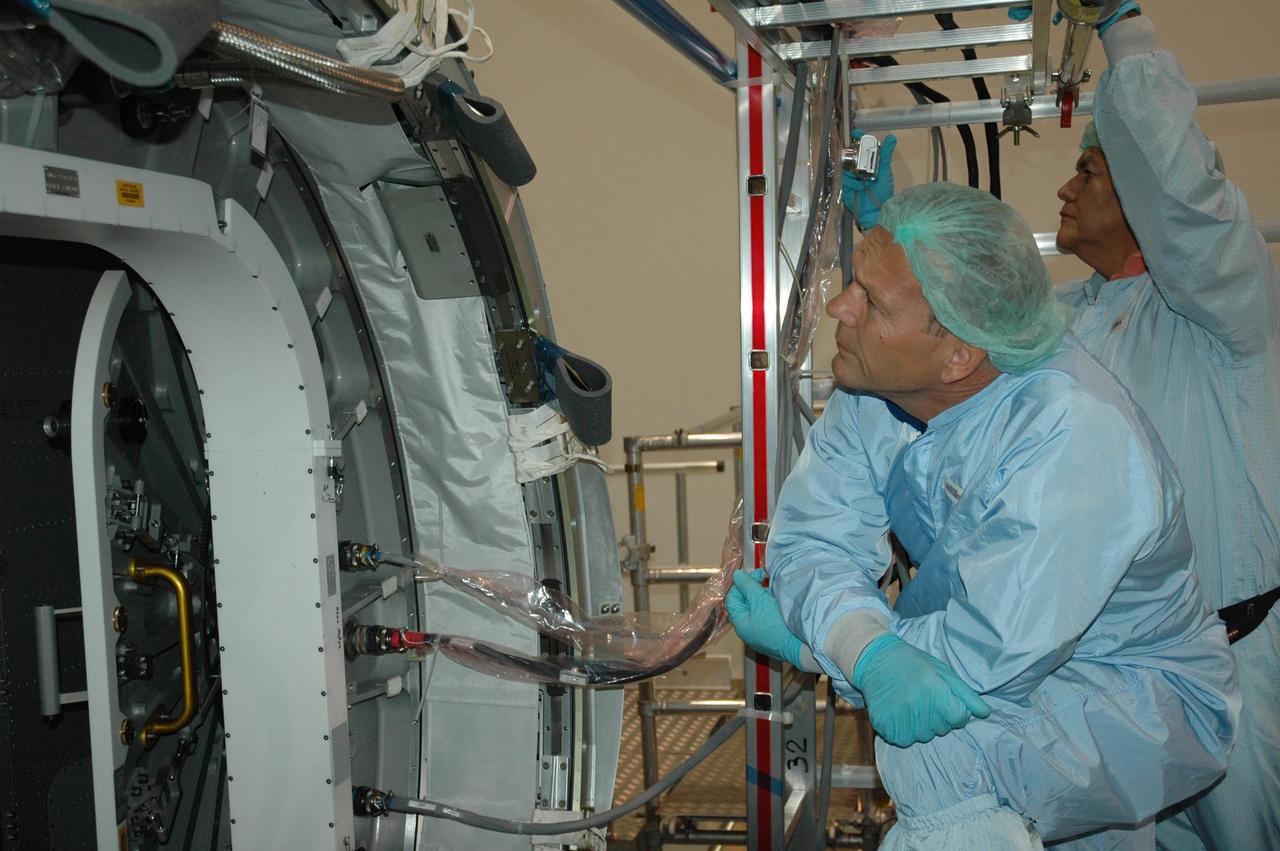 KENNEDY SPACE CENTER, FLA. STS-122 Mission Specialist Hans Schlegel looks closely at the hatch on the Columbus Research Laboratory in the Space Station Processing Facility. Schegel represents the European Space Agency. The crew is at Kennedy to take part in a crew equipment interface test, which helps familiarize them with equipment and payloads for the mission.  Among the activities standard to a CEIT are harness training, inspection of the thermal protection system and camera operation for planned extravehicular activities, or EVAs.  The Columbus Lab is Europe’s largest contribution to the construction of the International Space Station. It will support scientific and technological research in a microgravity environment. Columbus, a program of ESA, is a multifunctional, pressurized laboratory that will be permanently attached to Node 2 of the space station to carry out experiments in materials science, fluid physics and biosciences, as well as to perform a number of technological applications.  STS-122 is targeted for launch in December.   Photo credit: NASA/Jim Grossmann