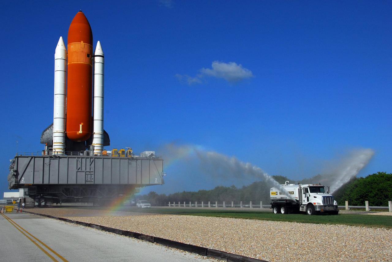 KENNEDY SPACE CENTER, FLA. -- A rainbow can be seen in the spray from the water truck traveling ahead of Space Shuttle Discovery on its move from the Vehicle Assembly Building to Launch Pad 39A. First motion out of the VAB was at 6:47 a.m. EDT. The water dampens the rocks on the crawlerway, reducing the amount of dust churned up by the passage of the shuttle. The crawler transporter carrying the mobile launch platform and unfueled space shuttle weighs approximately 17.5 million pounds. Rollout is a milestone for Discovery's launch to the International Space Station on mission STS-120, targeted for Oct. 23. The crew will be delivering and installing the Italian-built U.S. Node 2, named Harmony. The pressurized module will act as an internal connecting port and passageway to additional international science labs and cargo spacecraft. In addition to increasing the living and working space inside the station, it also will serve as a work platform outside for the station's robotic arm.   Photo credit: NASA/George Shelton