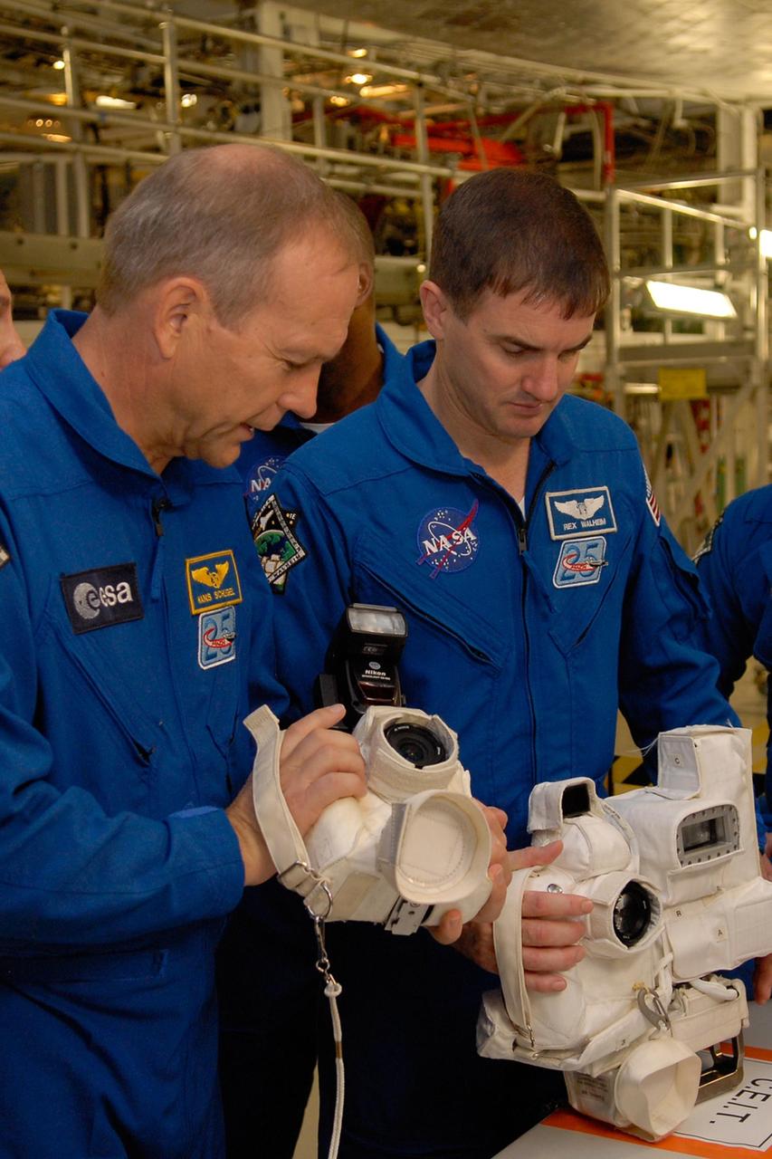 KENNEDY SPACE CENTER, FLA. --  In the Orbiter Processing Facility, members of the STS-122 crew look over cameras that will be used during the mission.  From left are Mission Specialists Hans Schlegel and Rex Walheim. Schlegel represents the European Space Agency. The crew is at Kennedy Space Center to take part in a crew equipment interface test, which helps familiarize them with equipment and payloads for the mission.  Among the activities standard to a CEIT are harness training, inspection of the thermal protection system and camera operation for planned extravehicular activities, or EVAs.  The mission will carry and install the Columbus Lab,  a multifunctional, pressurized laboratory that will be permanently attached to Node 2 of the space station to carry out experiments in materials science, fluid physics and biosciences, as well as to perform a number of technological applications. It is Europe’s largest contribution to the construction of the International Space Station and will support scientific and technological research in a microgravity environment.  STS-122 is targeted for launch in December.   Photo credit: NASA/Kim Shiflett