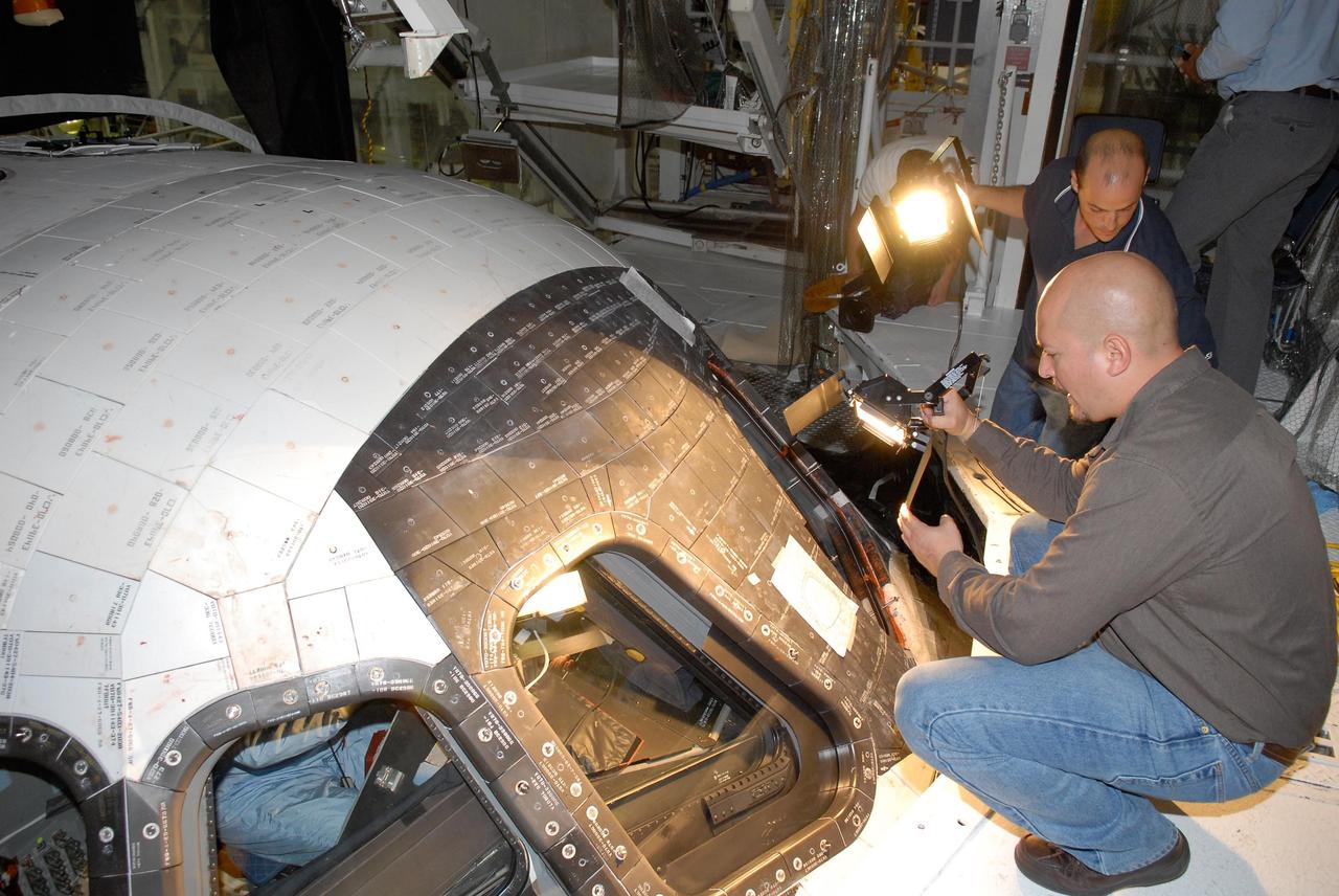 KENNEDY SPACE CENTER, FLA. -- In the Orbiter Processing Facility, United Space Alliance technicians provide lights over the space shuttle Atlantis' cockpit.  STS-122 Commander Stephen Frick is inside checking the cockpit for launch readiness.  The crew is at Kennedy Space Center to take part in a crew equipment interface test, which helps familiarize them with equipment and payloads for the mission.  Among the activities standard to a CEIT are harness training, inspection of the thermal protection system and camera operation for planned extravehicular activities, or EVAs.  The mission will carry and install the Columbus Lab,  a multifunctional, pressurized laboratory that will be permanently attached to Node 2 of the space station to carry out experiments in materials science, fluid physics and biosciences, as well as to perform a number of technological applications. It is Europe’s largest contribution to the construction of the International Space Station and will support scientific and technological research in a microgravity environment.  STS-122 is targeted for launch in December.   Photo credit: NASA/Kim Shiflett