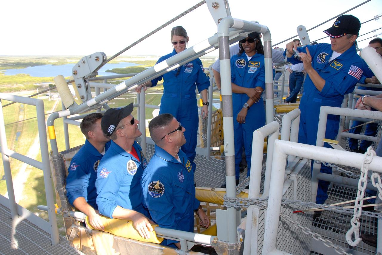 KENNEDY SPACE CENTER, FLA. -- The STS-120 crew is at NASA's Kennedy Space Center for the pre-launch terminal countdown demonstration test, or TCDT. Here, during emergency egress training, crew members practice climbing into the slidewire baskets that can carry them safely to a landing site away from the shuttle. In the basket are, from left, Mission Specialists Doug Wheelock and Scott Parazynski and Pilot George Zamka. Watching them are, from left, Commander Pamela Melroy and Mission Specialists Stephanie Wilson and Daniel Tani, with camera. After the mission, Tani will remain aboard the International Space Station and return with the STS-122 crew, targeted to launch Dec. 6. The TCDT provides astronauts and ground crews an opportunity to participate in various simulated countdown activities, including equipment familiarization and emergency training. The STS-120 mission will deliver the U.S. Node 2 module, named Harmony, aboard space shuttle Discovery to the International Space Station. Launch of Discovery on mission STS-120 is targeted for Oct. 23 at 11:38 a.m. EDT on a 14-day mission. Photo credit: NASA/Kim Shiflett