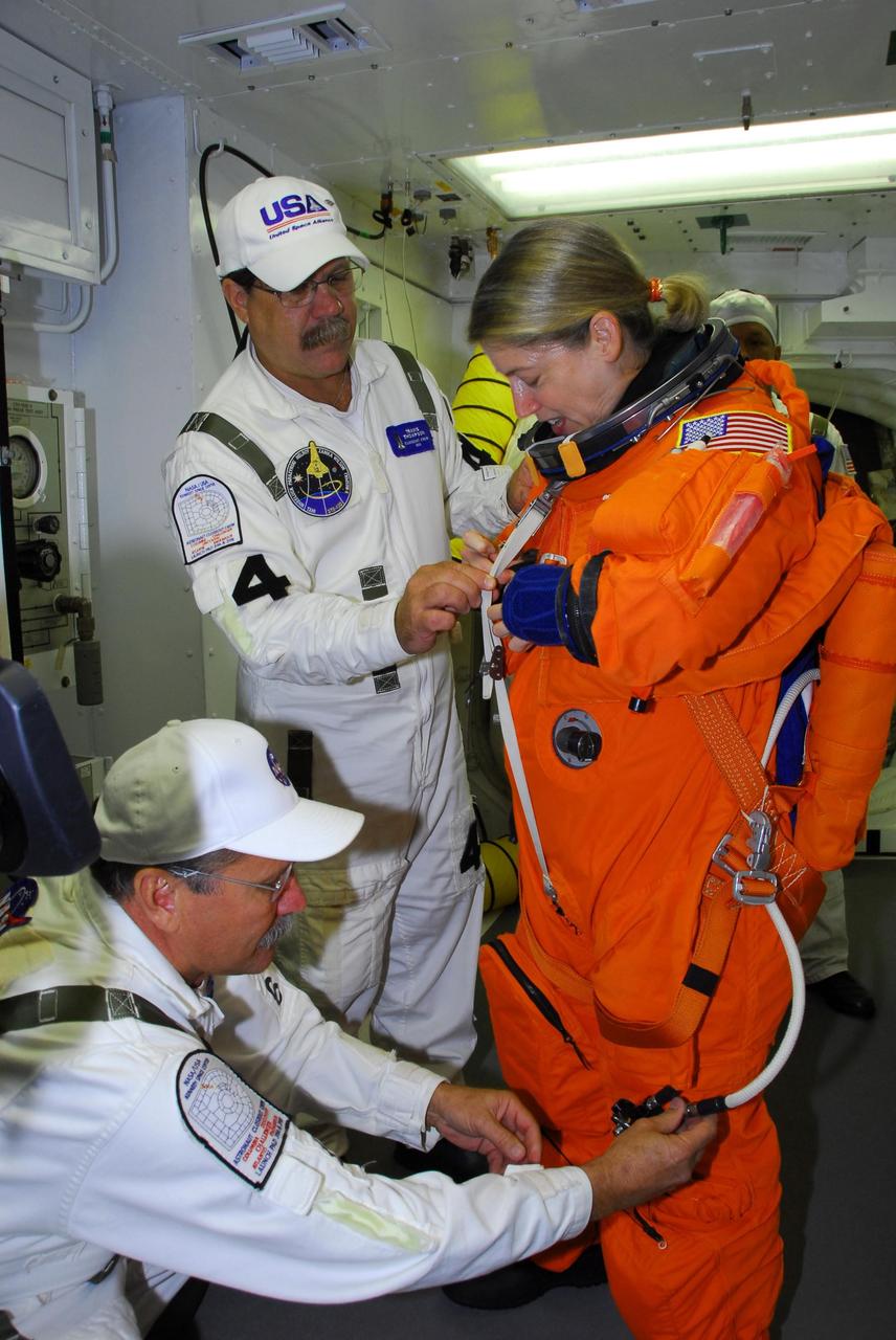 KENNEDY SPACE CENTER, FLA. -- In the white room on Launch Pad 39A, STS-120 Commander Pamela Melroy is helped by the closeout crew in donning a parachute pack before she crawls through the open hatch into space shuttle Discovery for a simulated launch countdown.  The countdown is the culmination of the prelaunch terminal countdown demonstration test, or TCDT.   The TCDT at NASA's Kennedy Space Center provides astronauts and ground crews an opportunity to participate in various launch preparation activities, including equipment familiarization and  emergency training. The STS-120 mission will deliver the U.S. Node 2 module, named Harmony, aboard space shuttle Discovery to the International Space Station.  Discovery is targeted to launch on its 14-day mission at 11:38 a.m. EDT on Oct. 23. Photo credit: NASA/George Shelton