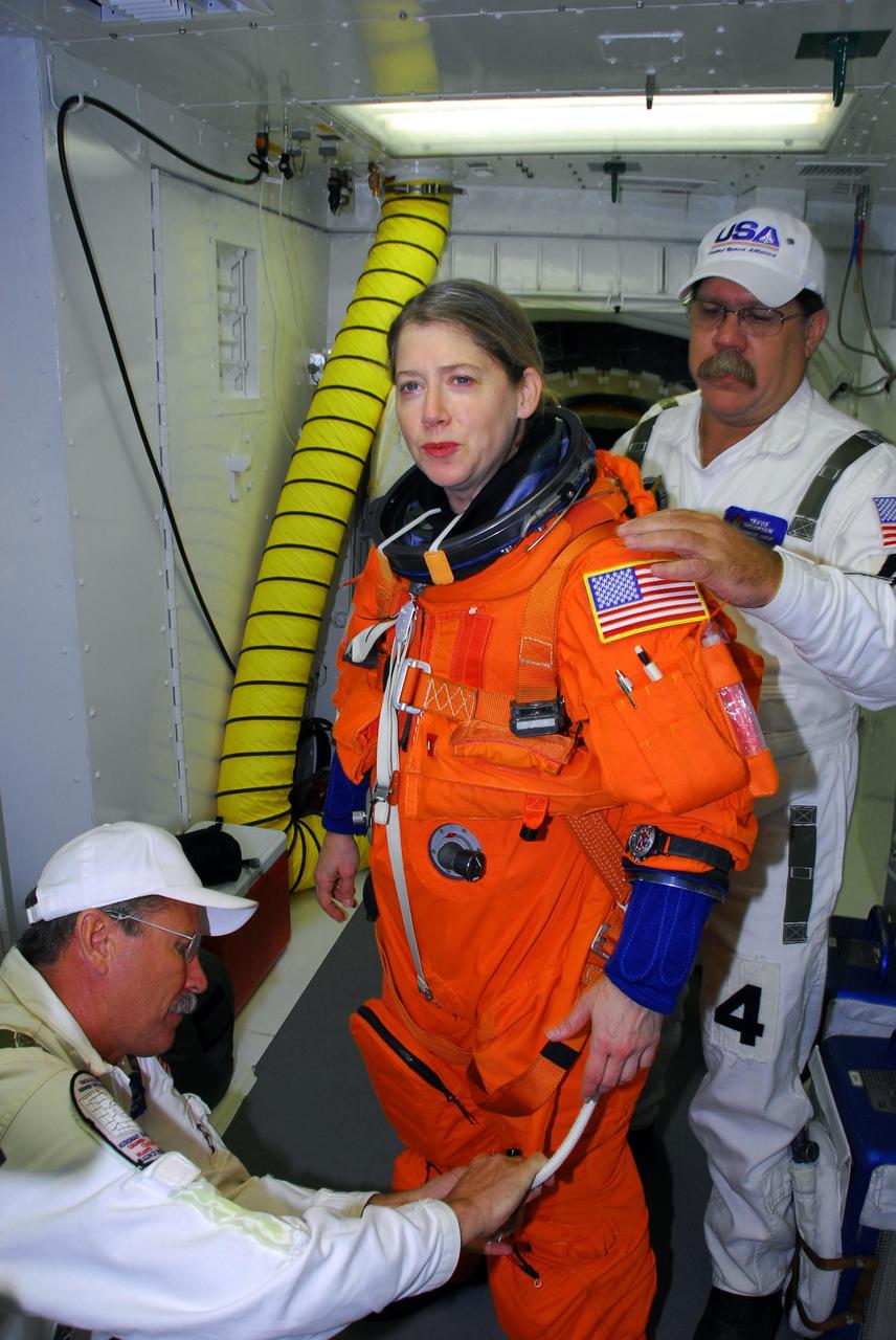 KENNEDY SPACE CENTER, FLA. -- In the white room on Launch Pad 39A, STS-120 Commander Pamela Melroy is helped by the closeout crew in donning a parachute pack before she crawls through the open hatch into space shuttle Discovery for a simulated launch countdown.  The countdown is the culmination of the prelaunch terminal countdown demonstration test, or TCDT.  Her name patch reflects the nicknames the crew gave each other for the event.  The TCDT at NASA's Kennedy Space Center provides astronauts and ground crews an opportunity to participate in various launch preparation activities, including equipment familiarization and  emergency training. The STS-120 mission will deliver the U.S. Node 2 module, named Harmony, aboard space shuttle Discovery to the International Space Station.  Discovery is targeted to launch on its 14-day mission at 11:38 a.m. EDT on Oct. 23. Photo credit: NASA/George Shelton