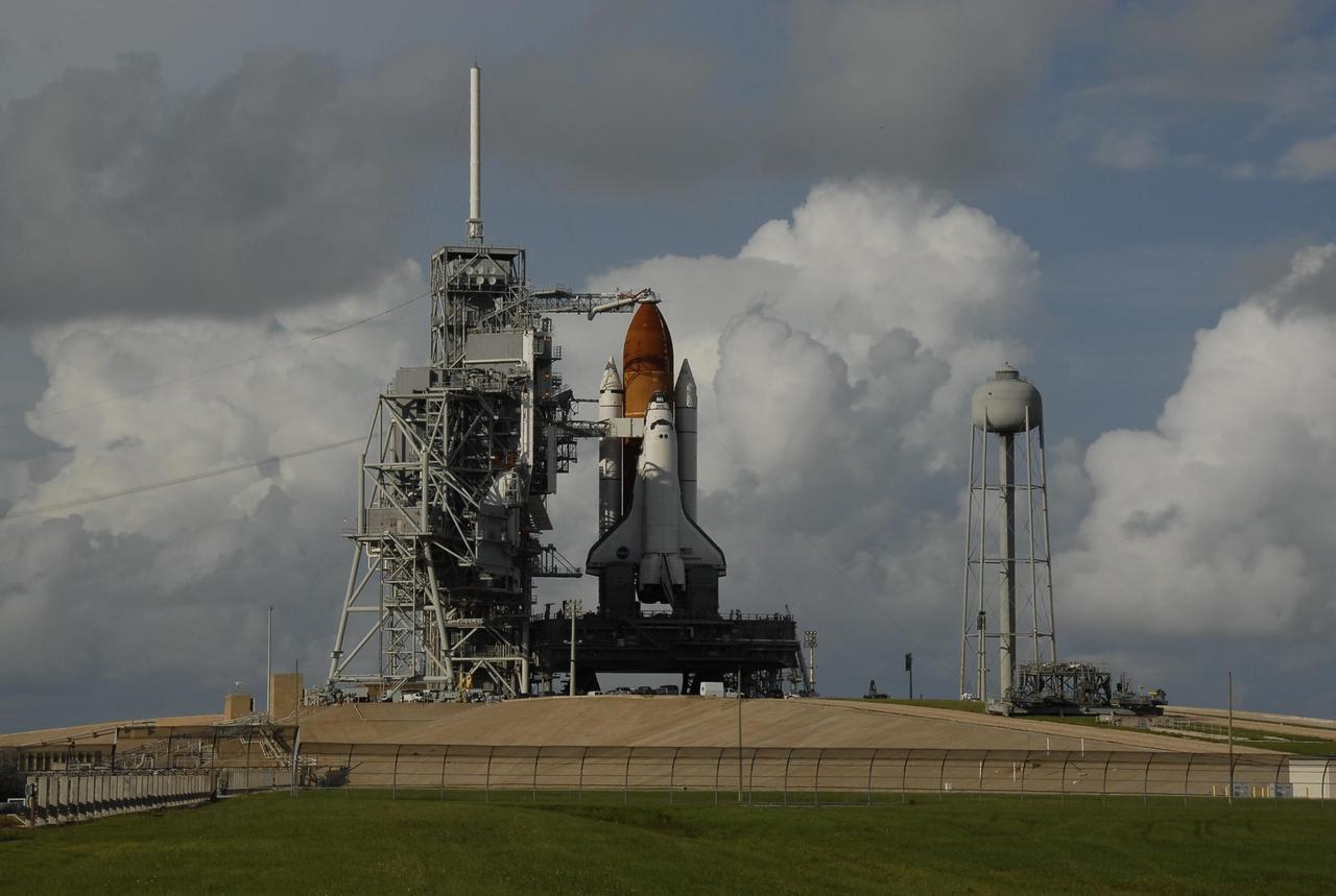 KENNEDY SPACE CENTER, FLA. -- Afternoon clouds have rolled in, serving as a background for space shuttle Discovery after rollback of the rotating service structure, at far left. Seen above the golden external tank is the vent hood (known as the "beanie cap") at the end of the gaseous oxygen vent arm, extending from the fixed service structure. Vapors are created as the liquid oxygen in the external tank boil off. The hood vents the gaseous oxygen vapors away from the space shuttle vehicle. Below it, also extending toward Discovery from the structure, is the orbiter access arm with the White Room at the end. The crew gains access into the orbiter through the White Room. At right is the 300,000-gallon water tank that provides water for sound suppression during liftoff. Rollback of the RSS started at 3:34 p.m. EDT and was complete at 4:20 p.m. The RSS provides protected access to the orbiter for changeout and servicing of payloads at the pad. Rollback of the pad's RSS is one of the milestones in preparation for the launch of mission STS-120. Discovery is scheduled for liftoff at 11:38 a.m. EDT on Oct. 23. The mission will be the 23rd assembly flight to the International Space Station and the 34th flight for Discovery. Payload on the mission is the Italian-built U.S. Node 2, called Harmony. The 14-day mission will install Harmony and move the P6 solar arrays to their permanent position and deploy them. Discovery is expected to complete its mission and return home at 4:47 a.m. EST on Nov. 6. Photo credit: NASA/Kim Shiflett